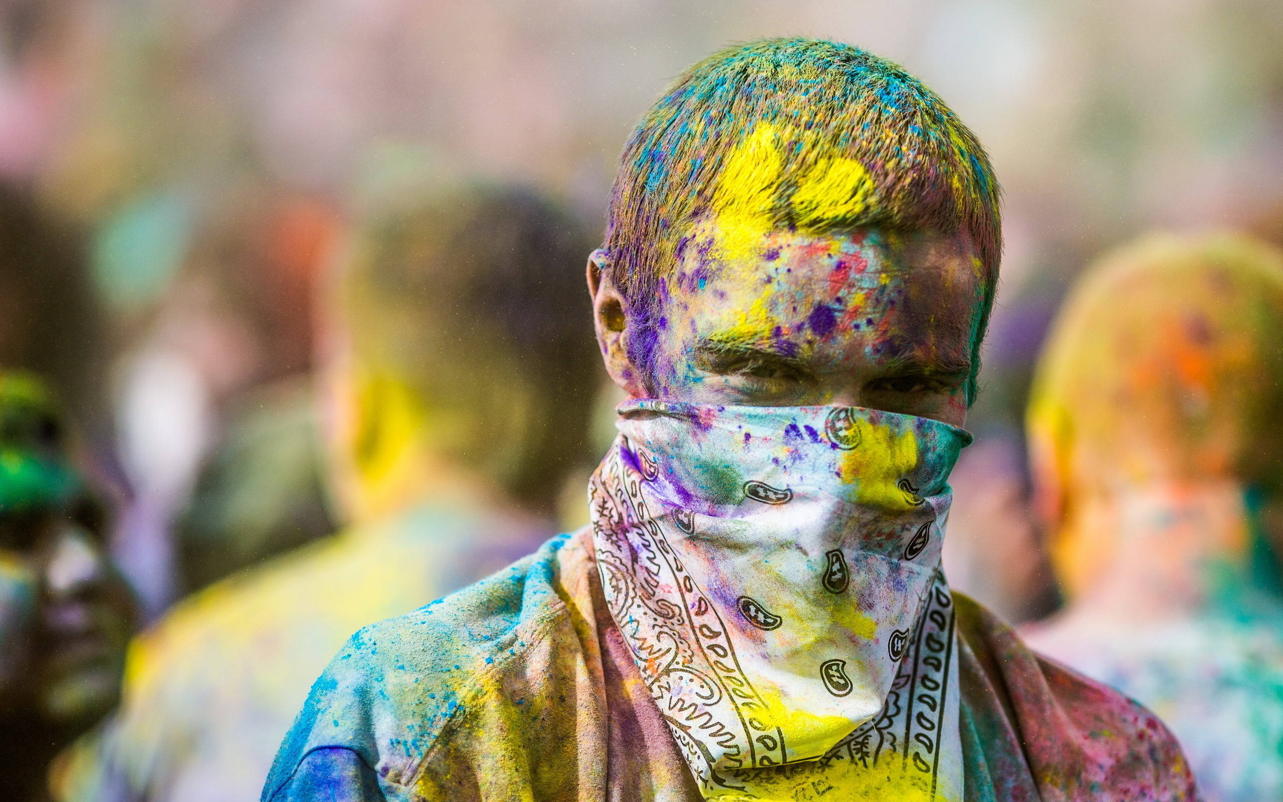 Holi 桌布 壁紙 — 一個人在節日慶祝活動中，全身佈滿鮮豔的粉末顏色，背景有模糊的參與者。