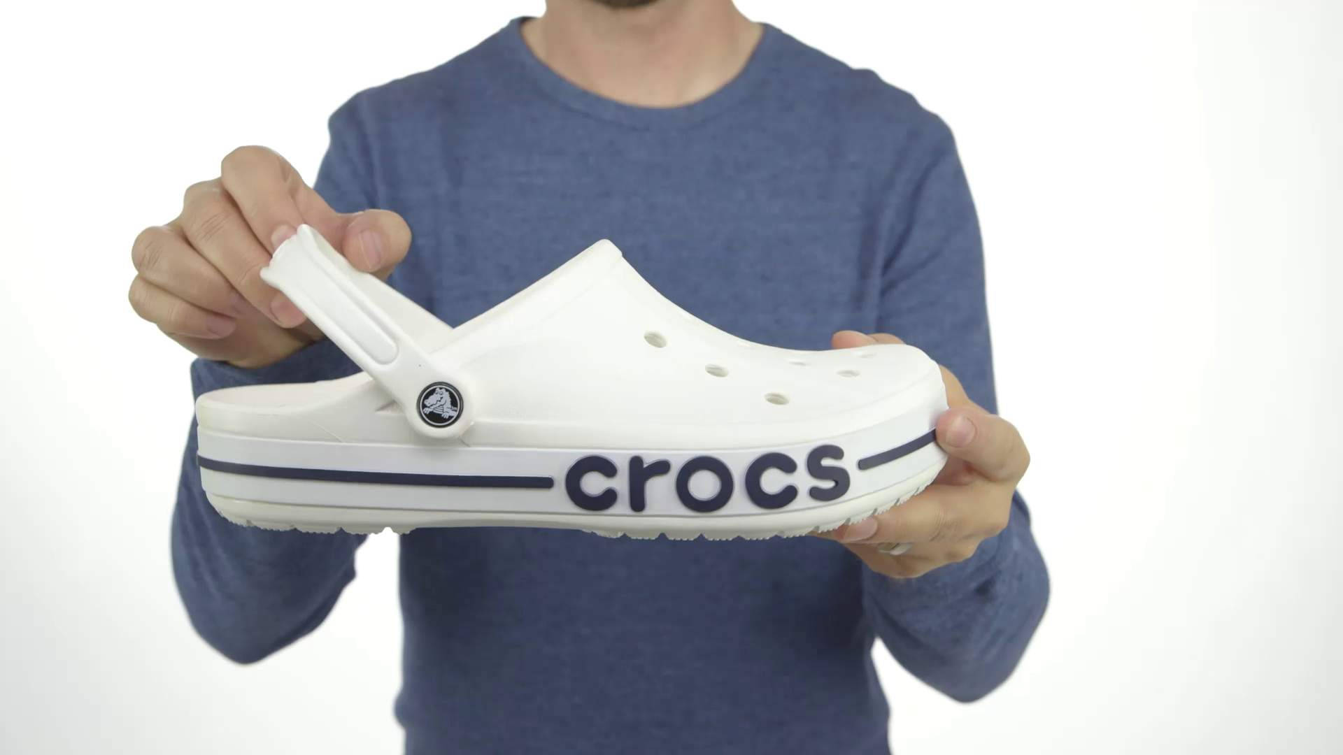 Crocs 桌布 壁紙 — 一個人在純白背景前，拿著一隻白色Crocs木屐，上面有海軍藍色品牌標誌。
