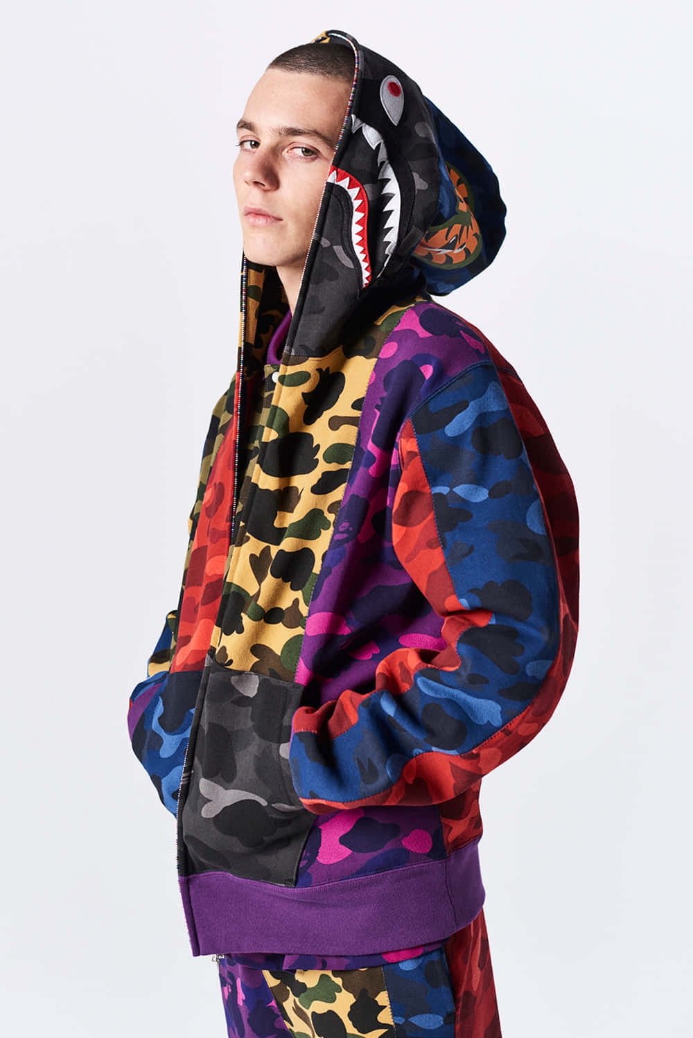 Bape 動態 桌布 壁紙 — 一個人在純白色背景上穿著鮮豔的多圖案連帽衫，帶有鯊魚頭帽。