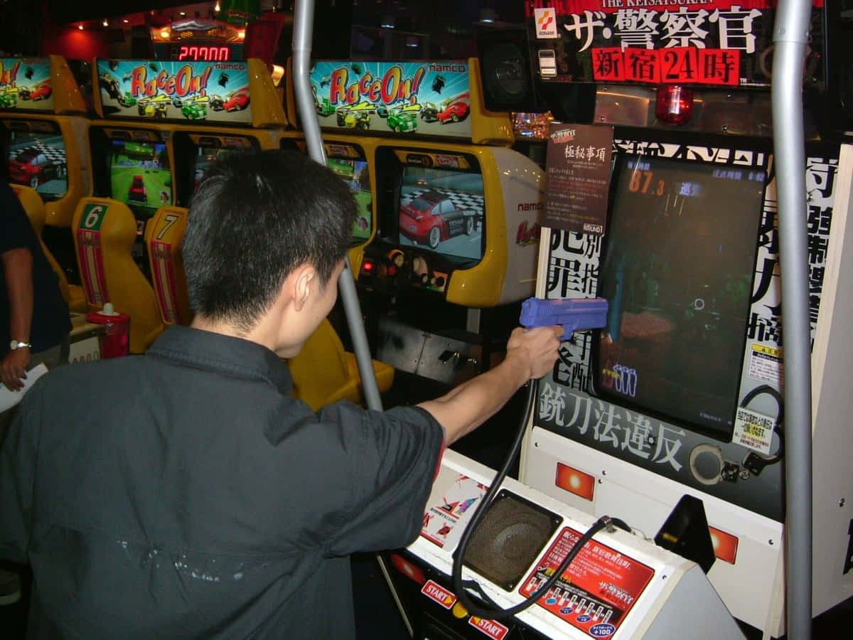 Arcade Games 桌布 壁紙 — 一個人在繁忙的日本遊戲機中心用光槍玩賽車街機遊戲，周圍充滿色彩繽紛的機台。