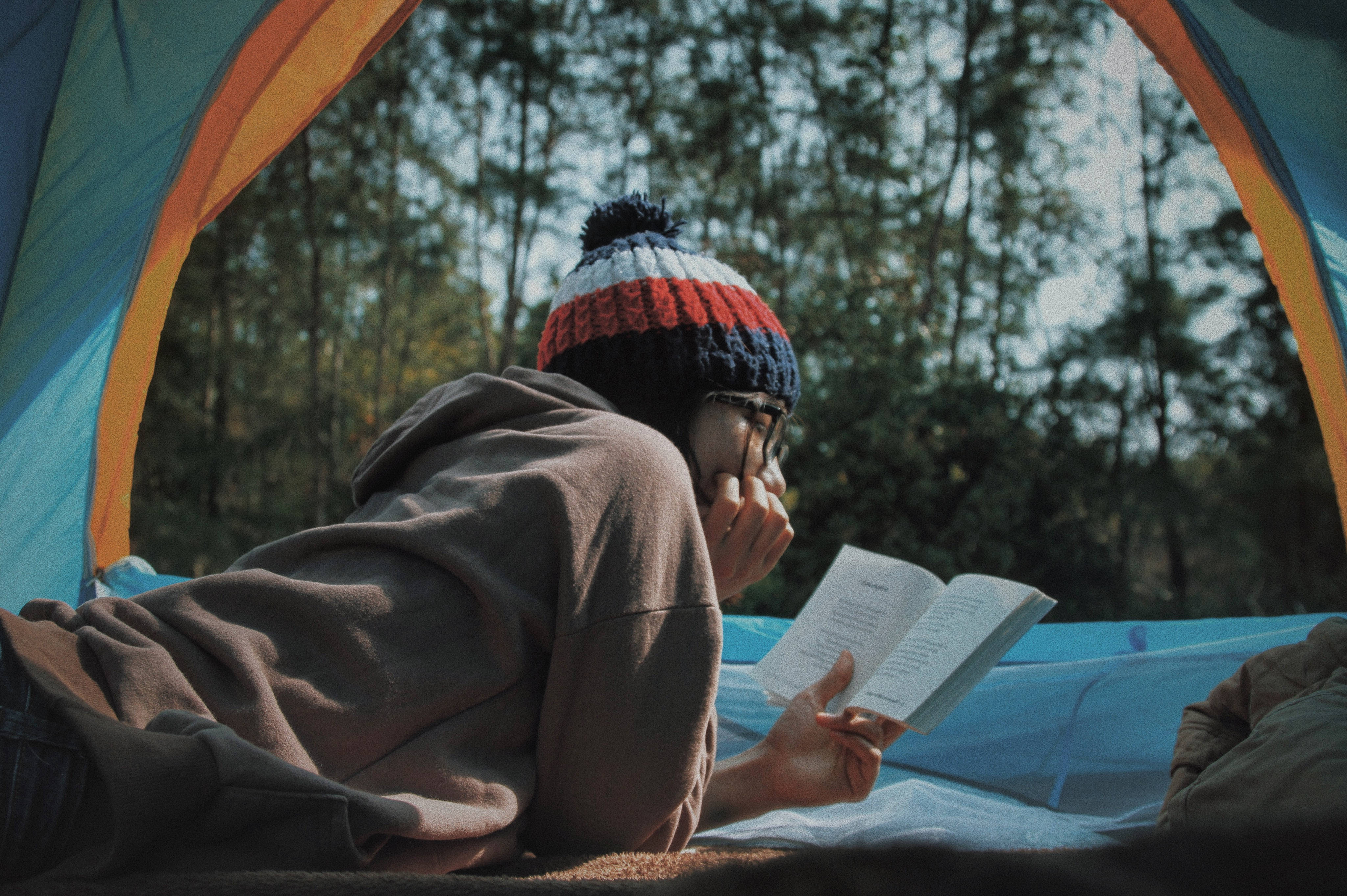 看書 桌布 壁紙 — 一個人在色彩繽紛的帳篷裡看書，被寧靜森林中的高大樹木包圍。