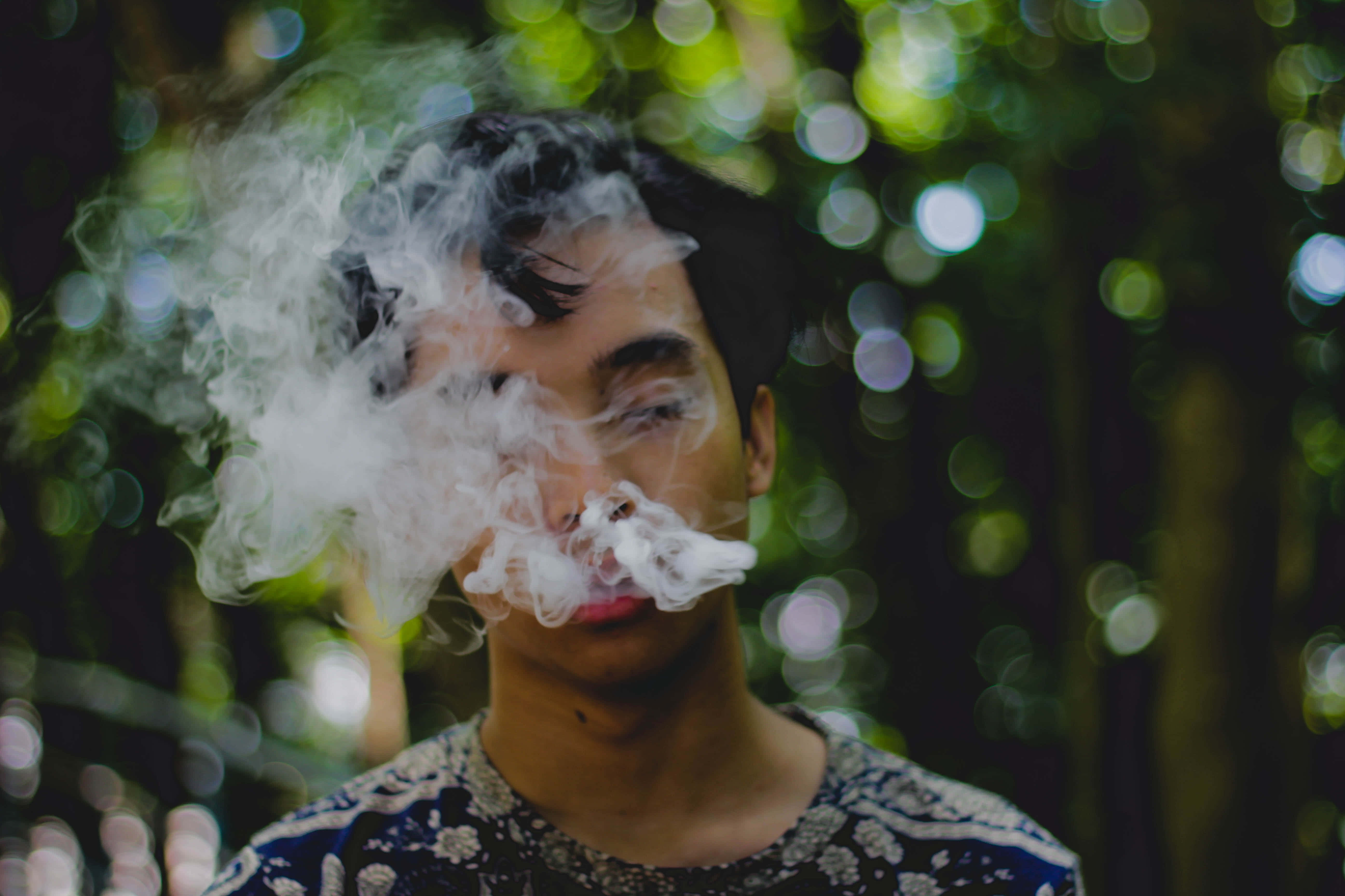 Man 桌布 壁紙 — 一個人在茂密的綠色森林背景和散景燈光下呼出濃厚的白煙，煙霧在他們的臉龐周圍旋轉。