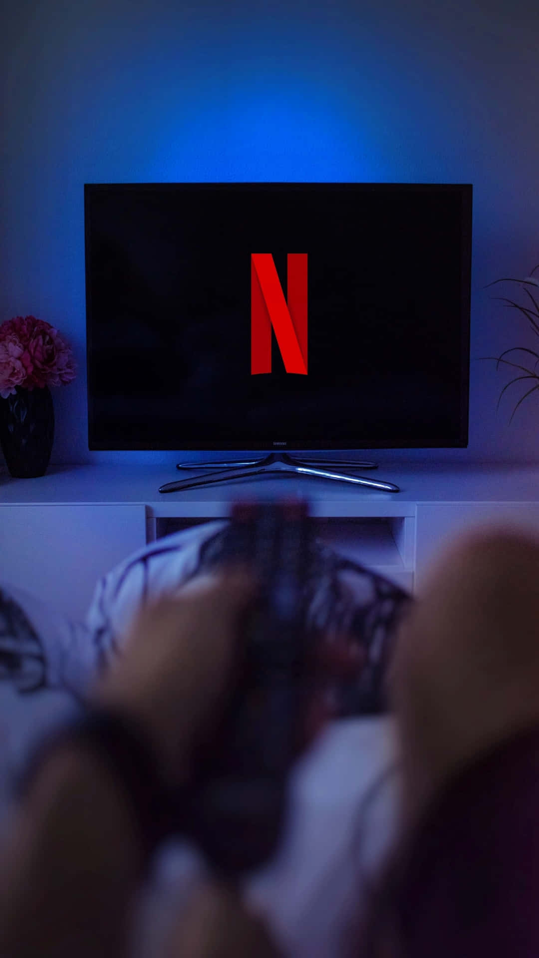 Streaming Service 桌布 壁紙 — 一個人在藍色環境燈光下，在顯示Netflix標誌的電視前用控制器玩電子遊戲。