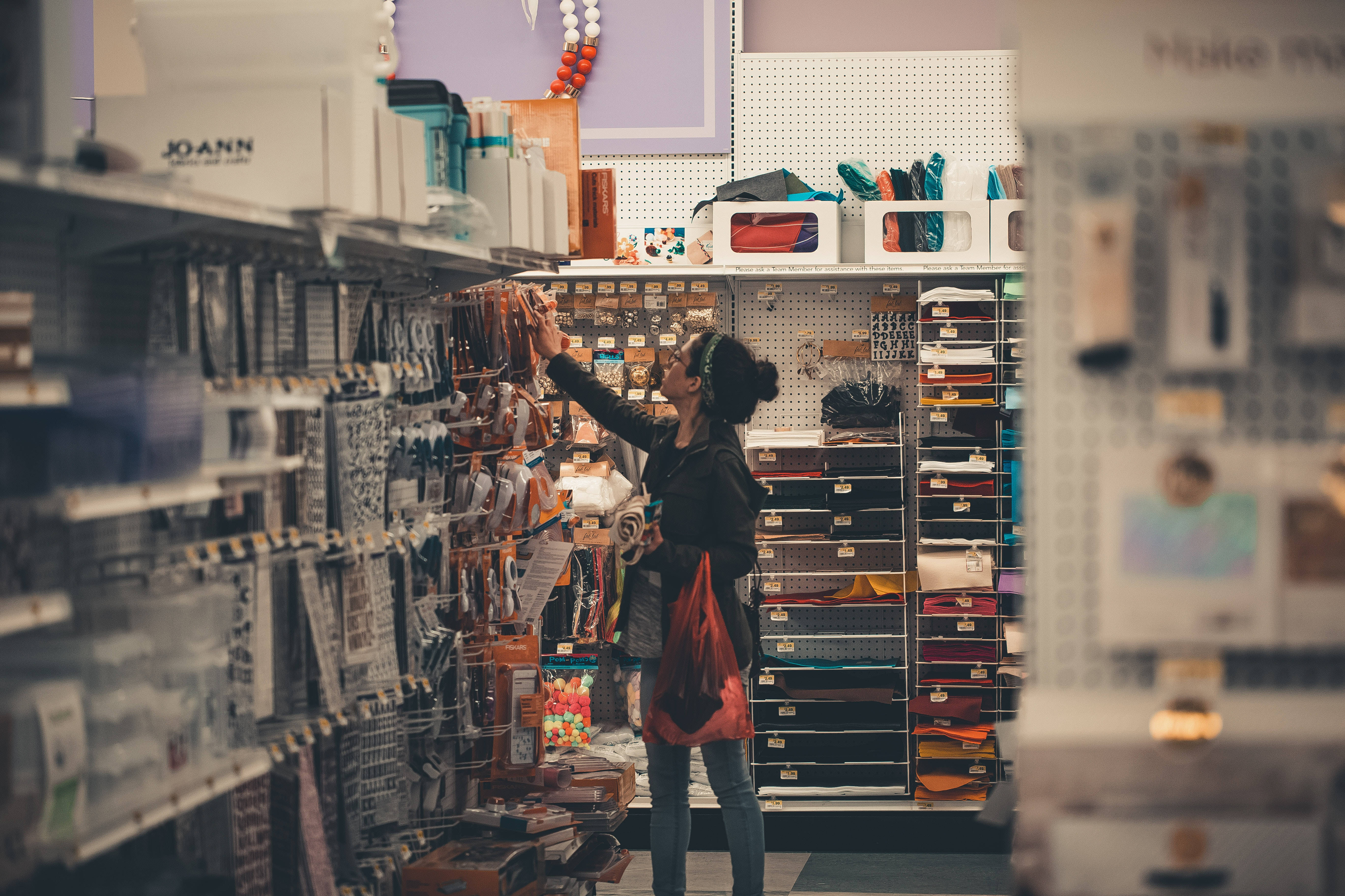 Woman 桌布 壁紙 — 一個人在貨品齊全的藝術用品店通道中，伸手去拿高架上的手工藝用品。