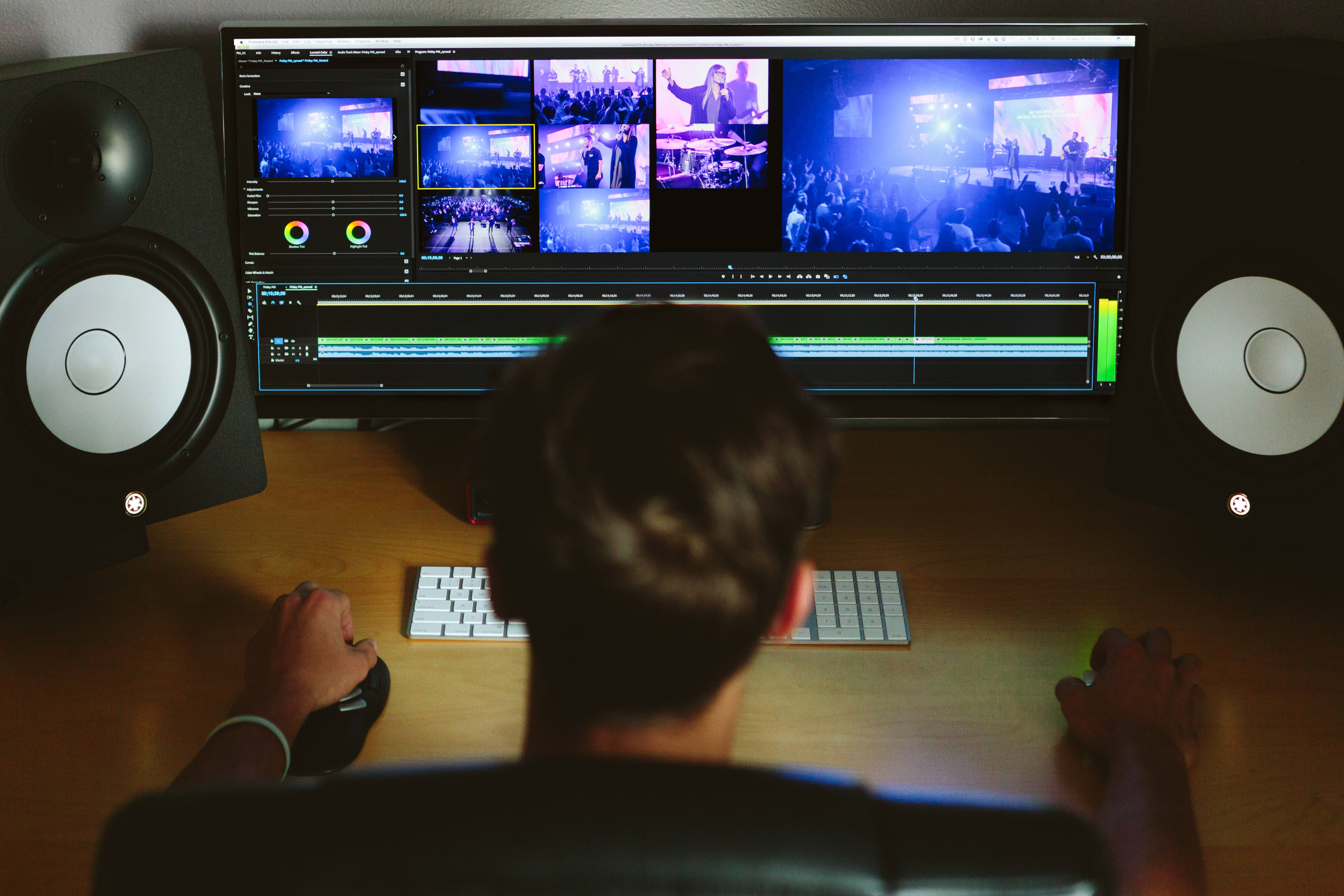 Editing 桌布 壁紙 — 一個人在辦公桌前編輯大型顯示器上的現場音樂會片段，顯示器兩側有錄音室喇叭。