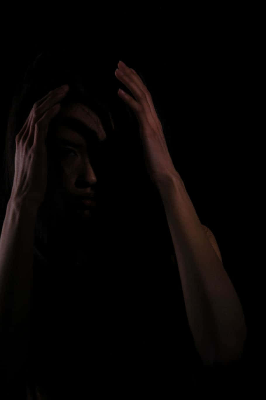 Dark Fear 桌布 壁紙 — 一個人在近乎黑暗的環境中，用雙手抱住頭部，被單一戲劇性的光源照亮。