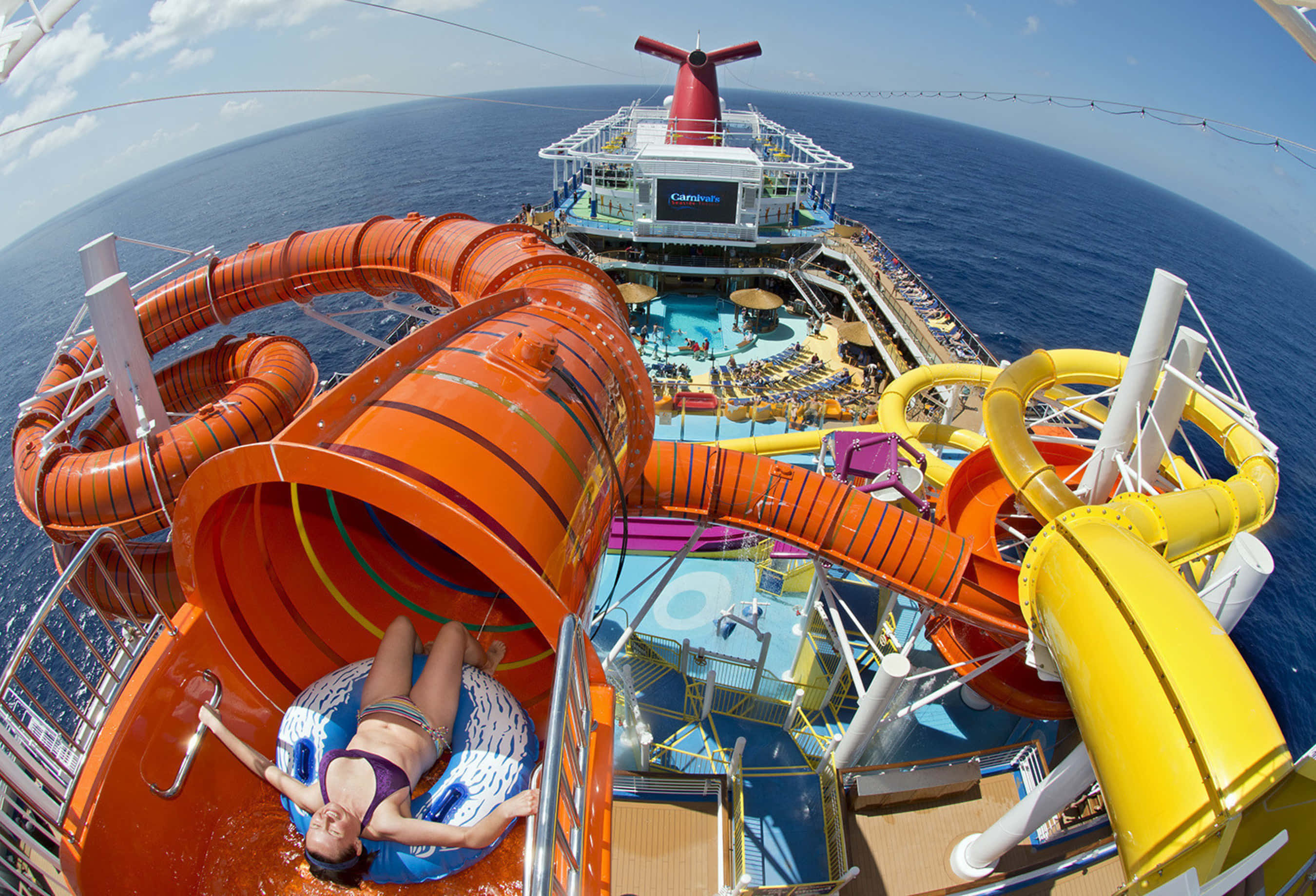 Carnival Conquest 桌布 壁紙 — 一個人在郵輪上沿著亮橙色的水上滑梯滑下，下方可見海洋和甲板泳池。