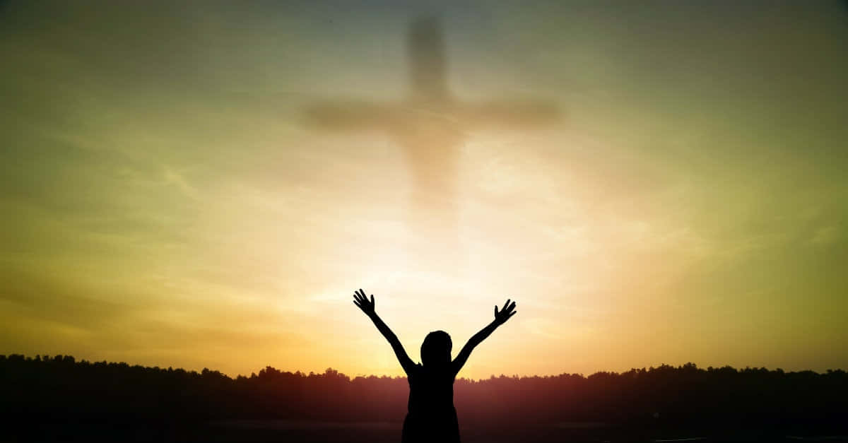Gospel 桌布 壁紙 — 一個人在金色夕陽天空下，於發光十字架下舉起雙臂敬拜的剪影。