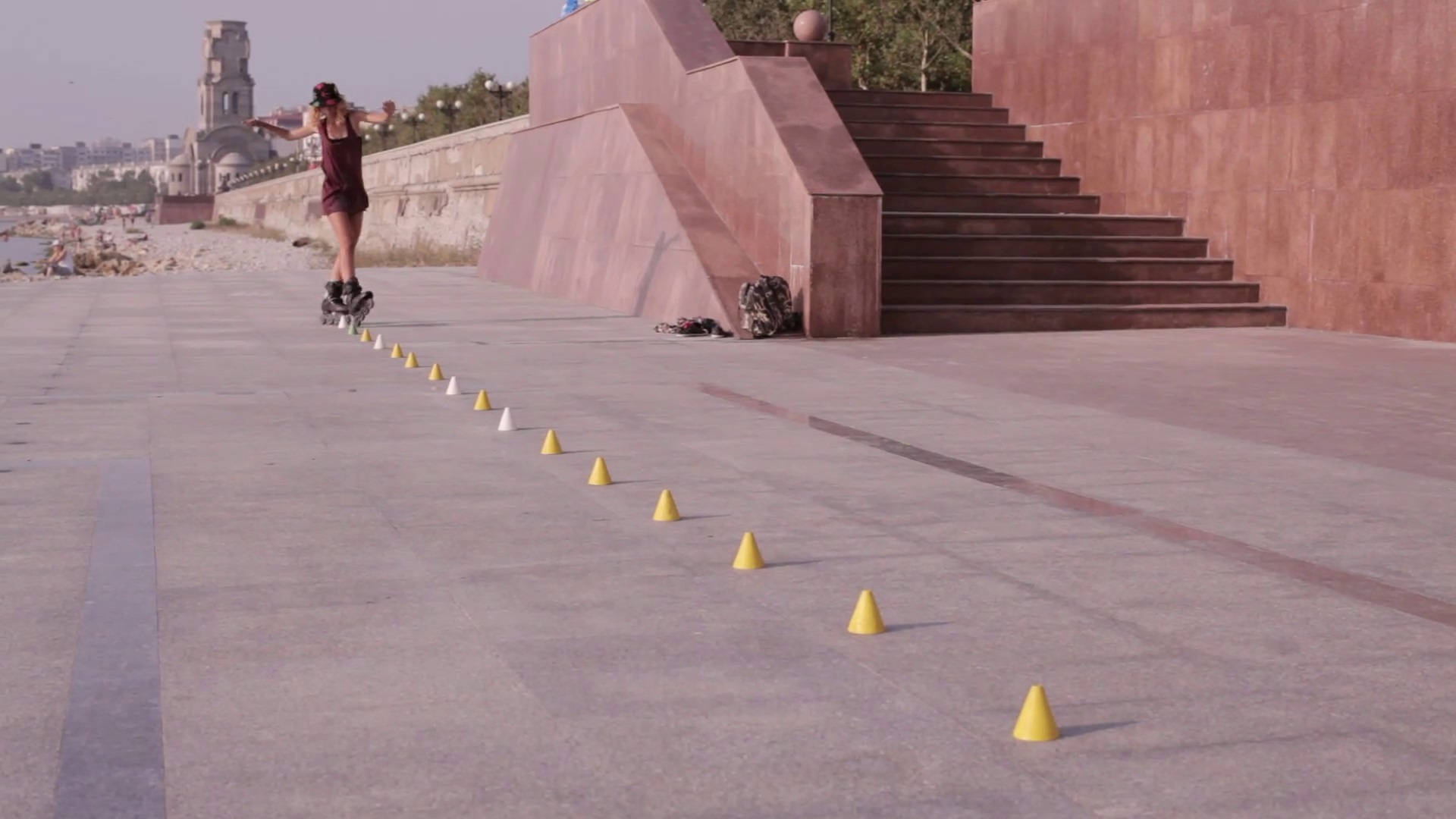 skating 桌布 壁紙 — 一個人在鋪砌的廣場上穿過一排黃色錐體，旁邊有現代樓梯和遠處的塔樓，踩著直排輪。