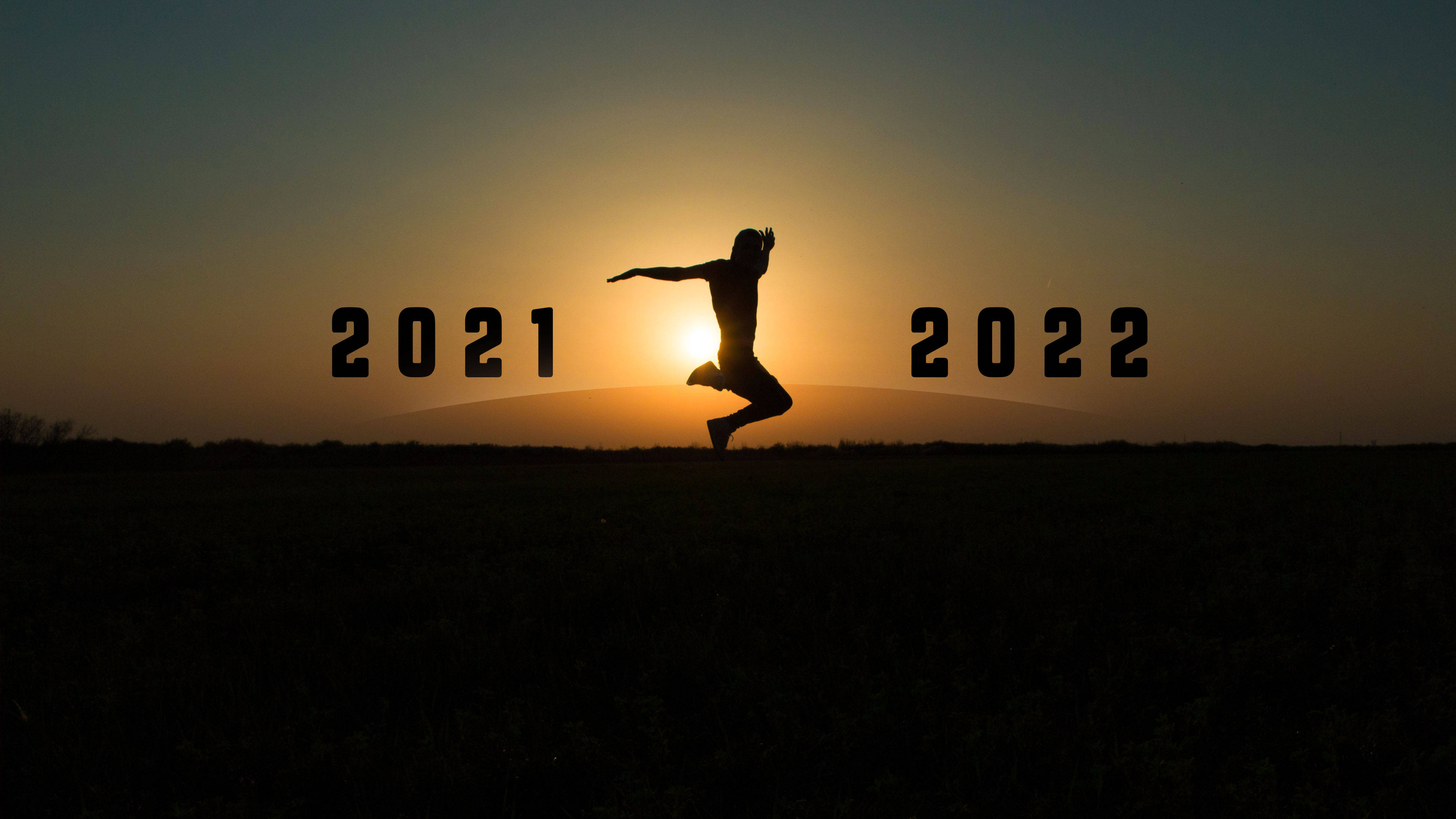 Happy New Year 2022 桌布 壁紙 — 一個人在閃爍的日落地平線背景下，歡樂地跳躍於2021年和2022年之間。