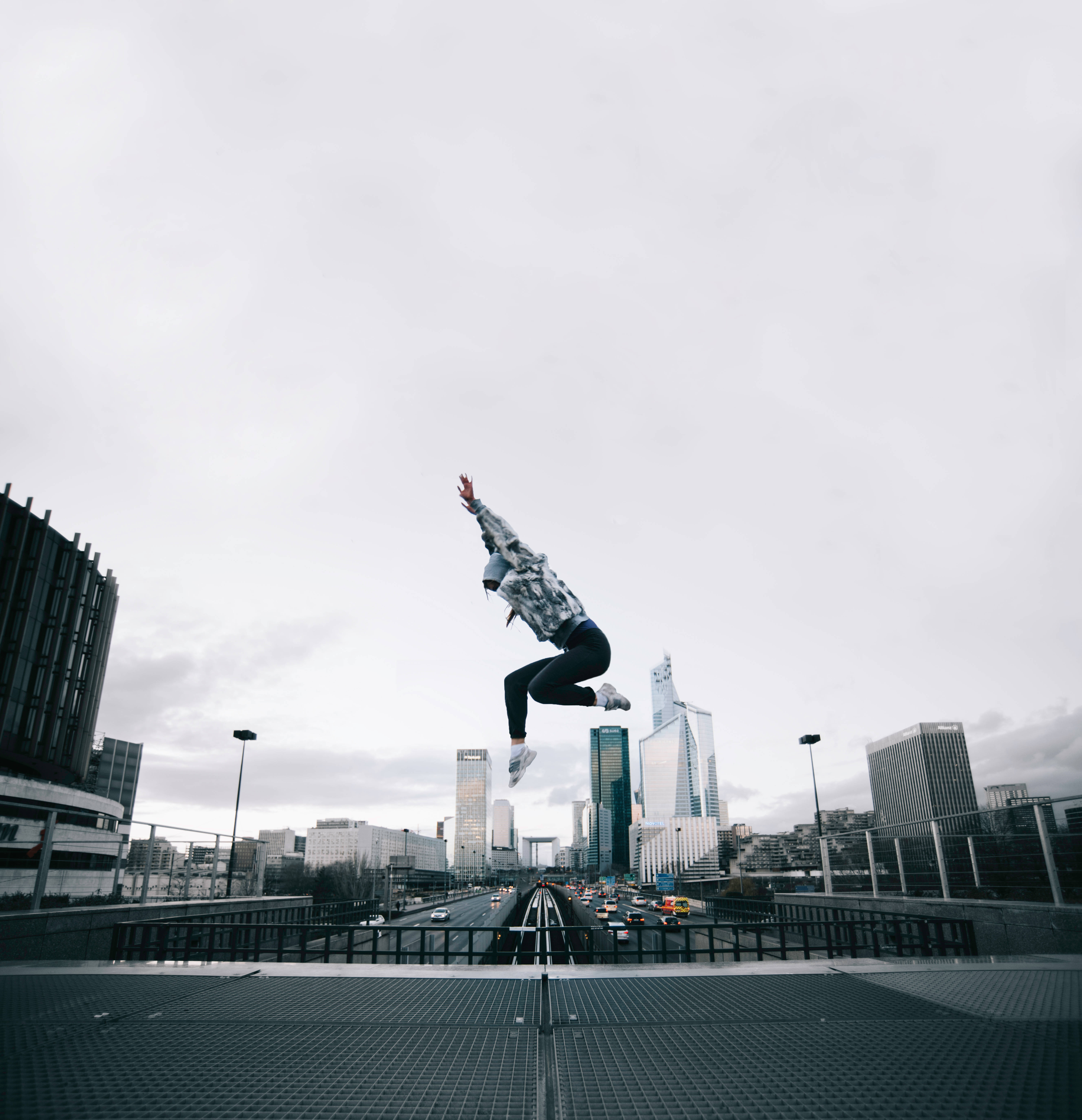 Jumping 桌布 壁紙 — 一個人在陰天下的城市高速公路上方跳躍，背景有現代摩天大樓。