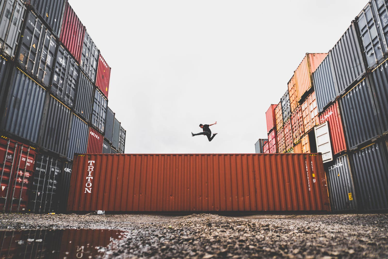 Jumping 桌布 壁紙 — 一個人在陰天的工業場地，在堆疊的貨櫃之間，凌空跳過一個紅色貨櫃。