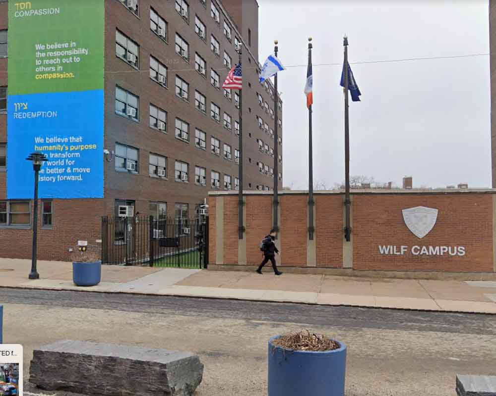 建築 桌布 壁紙 — 一個人在陰天走過一面磚牆，牆上有『WILF CAMPUS』標誌和四面旗幟。