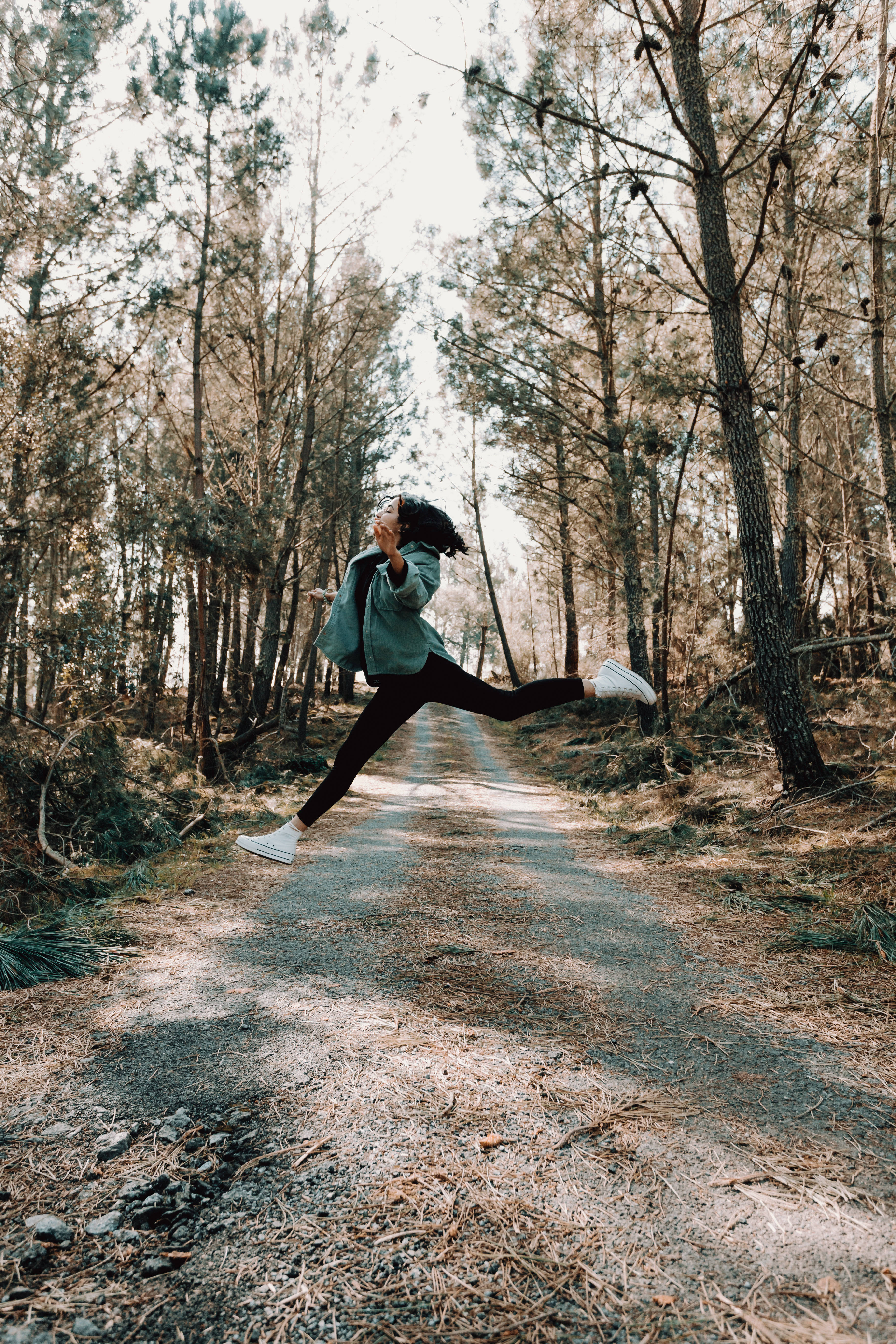 Jumping 桌布 壁紙 — 一個人在陽光普照的森林小徑上快樂地跳躍，周圍是高聳的松樹和斑駁的陰影。