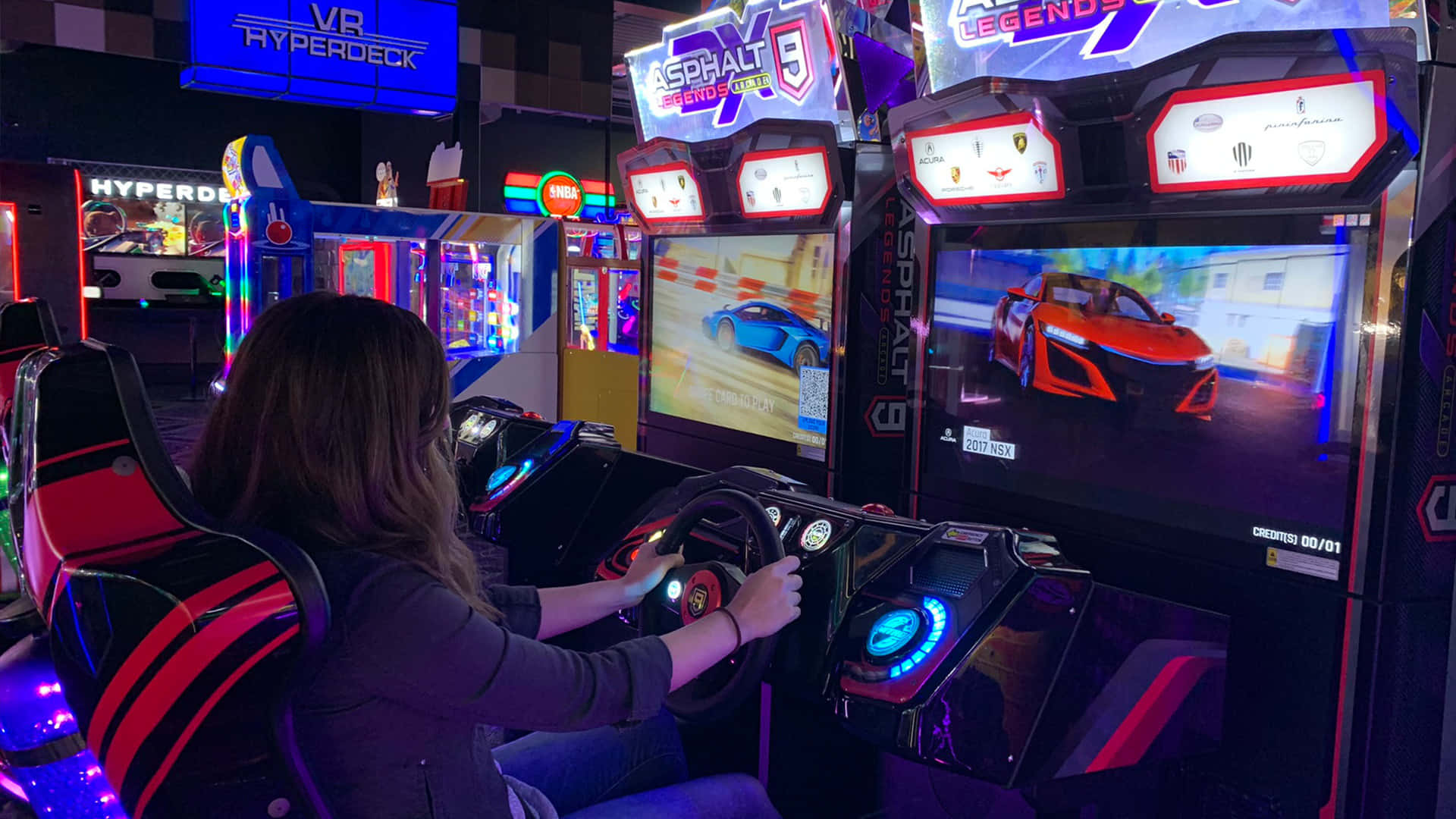 Arcade Games 桌布 壁紙 — 一個人在霓虹燈光閃爍的遊戲機中心玩賽車街機遊戲，控制台發光，螢幕色彩鮮豔。