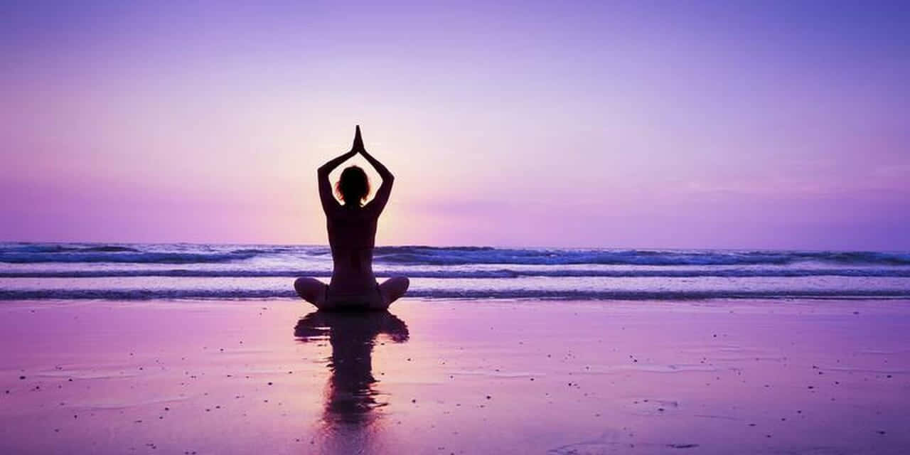 Spiritual Awakening 桌布 壁紙 — 一個人在黃昏時分在濕漉漉的海灘上以瑜伽姿勢冥想，紫色天空和海洋波浪的剪影。