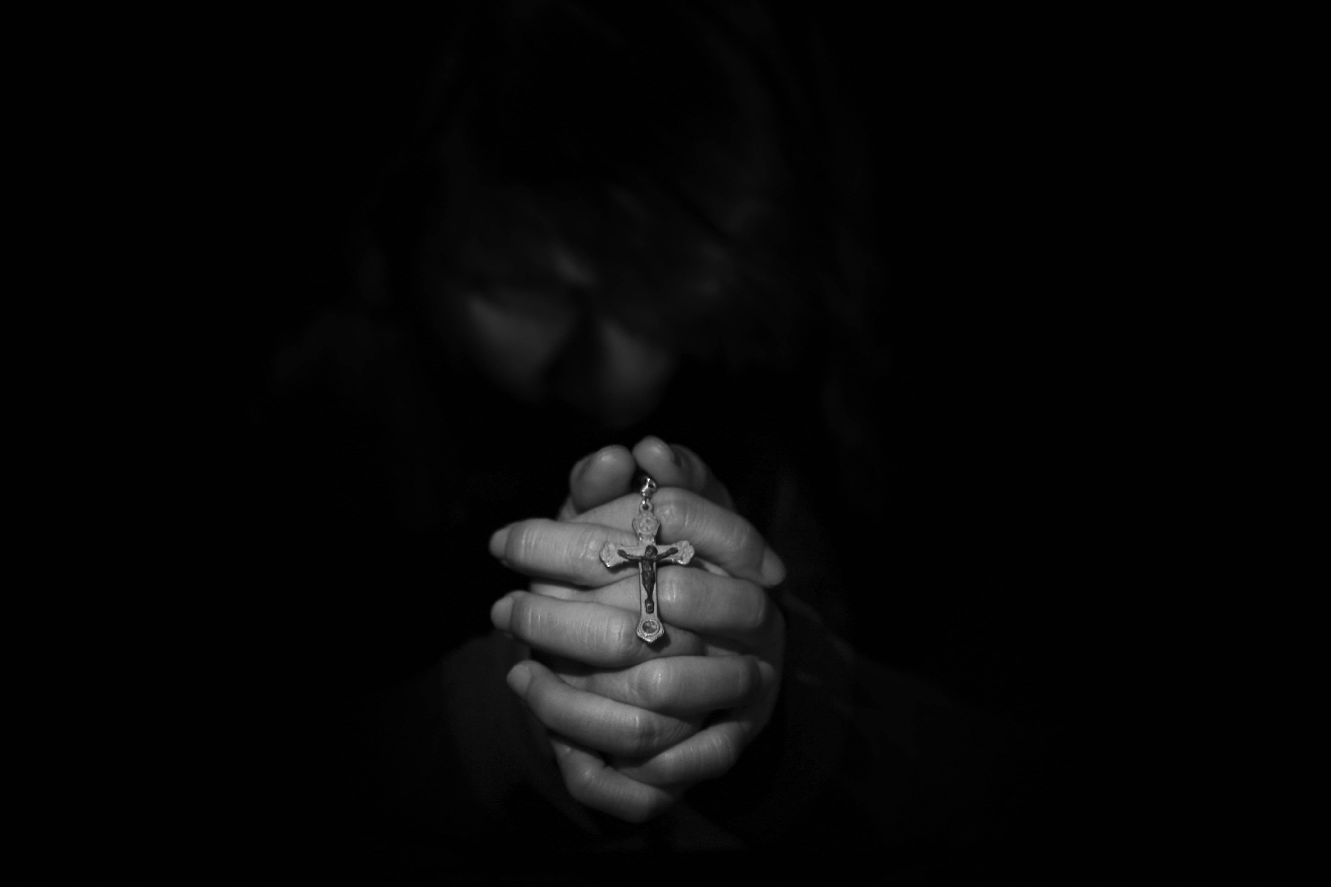 Praying Hands 桌布 壁紙 — 一個人在黑暗中雙手合十握著十字架，臉龐在莊嚴的祈禱中隱藏。