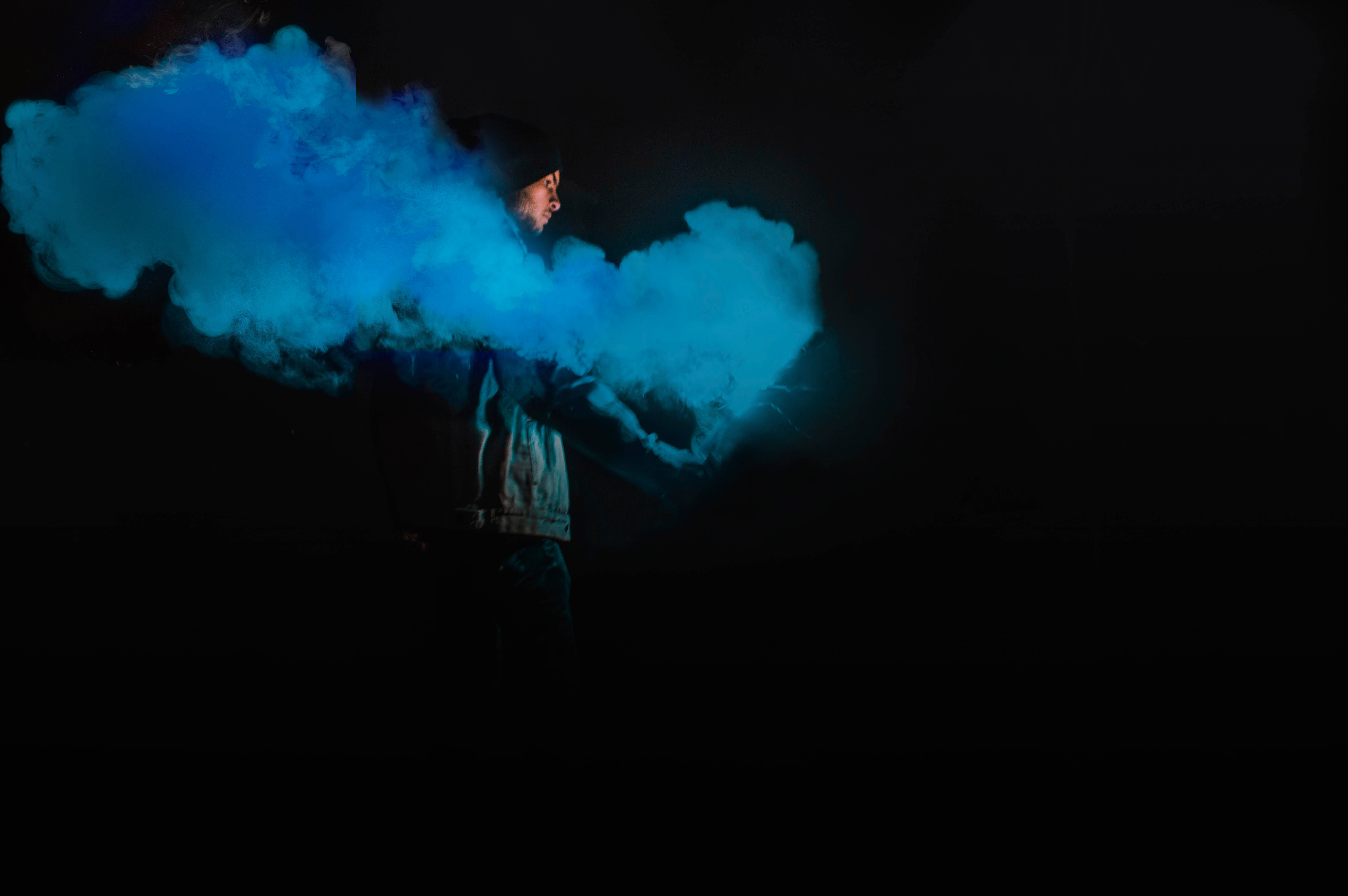 Smoking 桌布 壁紙 — 一個人在黑暗環境中呼出一團充滿活力的藍色蒸氣雲，照亮了他們的臉和外套。