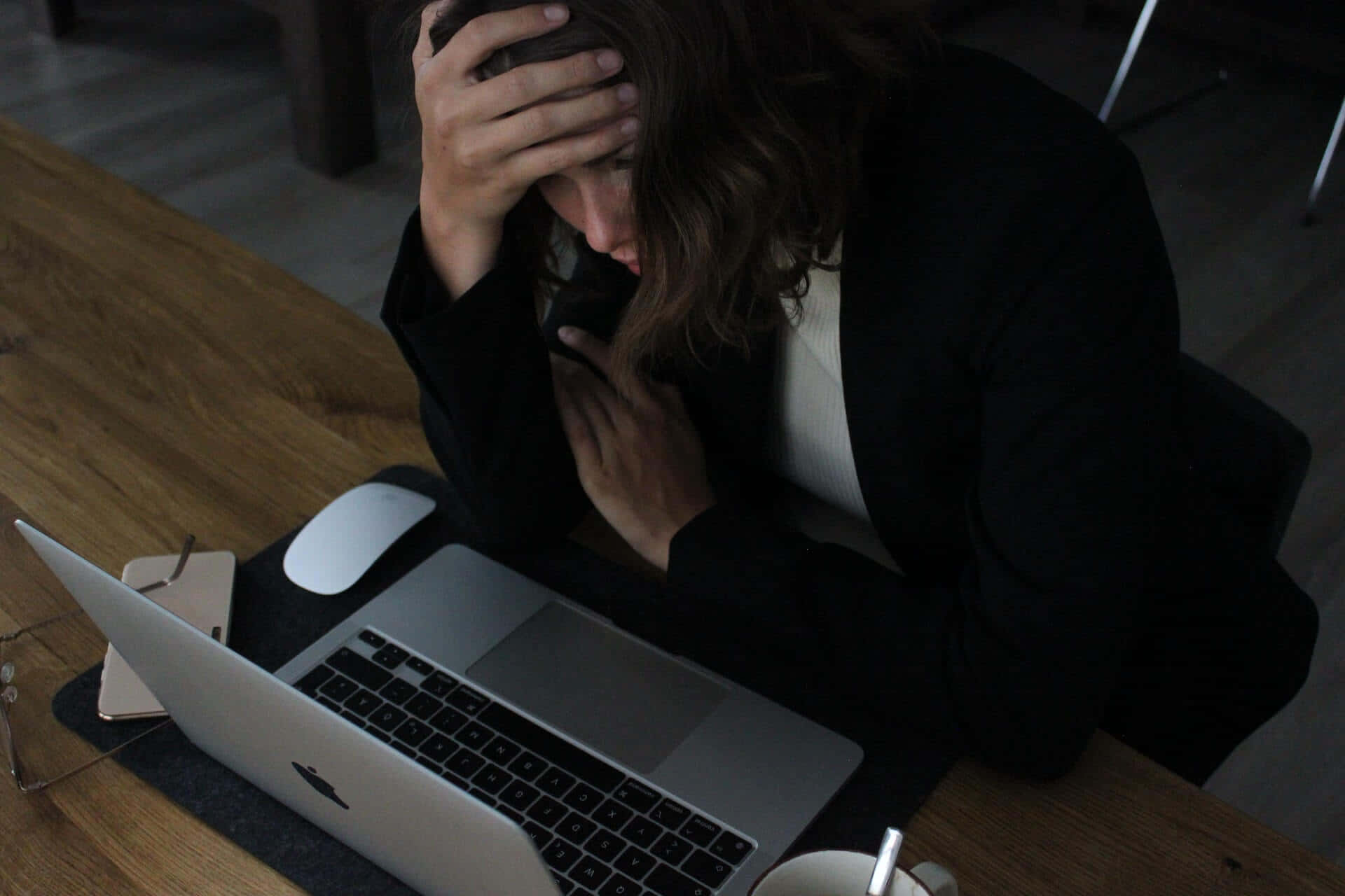 Stress 桌布 壁紙 — 一個人在黑暗的房間裡俯身於筆記型電腦上，雙手抱頭，似乎被工作壓力壓得喘不過氣。