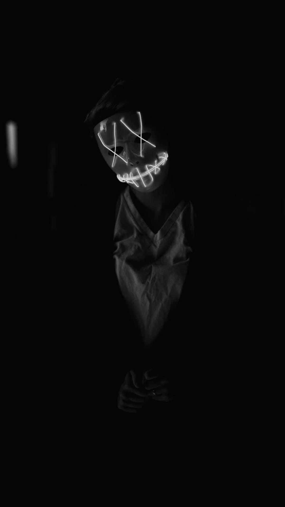 Goth Aesthetic Black 桌布 壁紙 — 一個人在黑暗的房間裡戴著一個發光的白色LED面具，面具上有鋸齒狀線條形成邪惡的笑容。