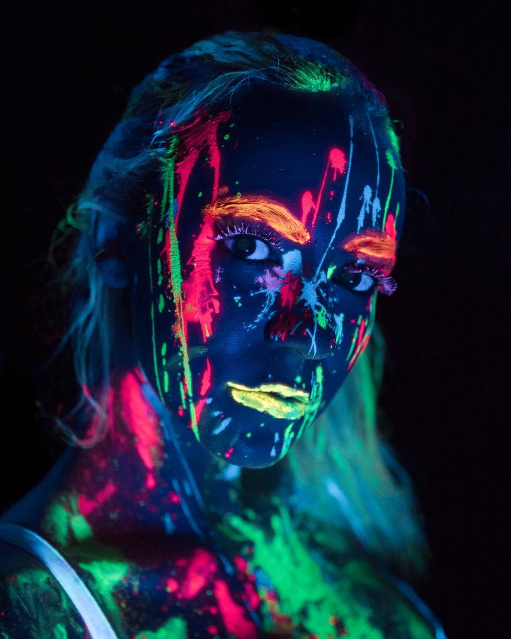 Trippy Dark 桌布 壁紙 — 一個人在黑暗背景下，於黑光下臉部和頸部帶有發光霓虹顏料條紋。