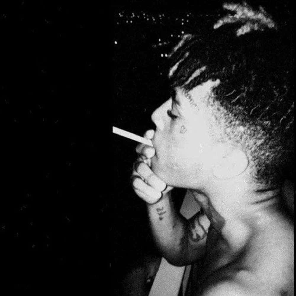 酷酷的xxxtentacion 桌布 壁紙 — 一個人在黑暗背景中吸煙的黑白特寫，背景有星狀斑點。