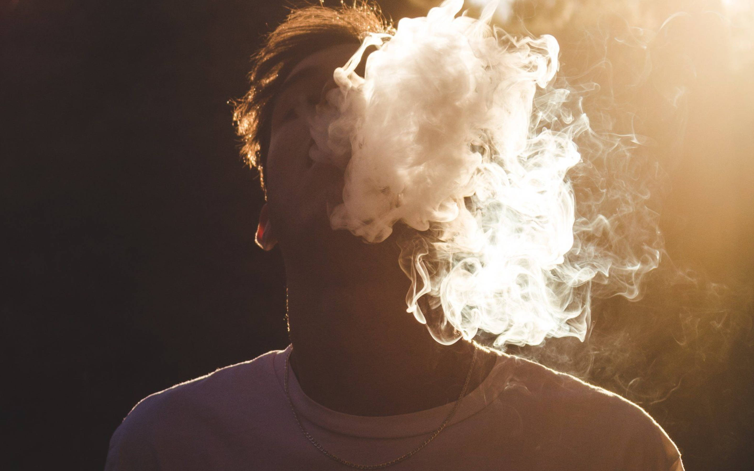 吸大麻 桌布 壁紙 — 一個人在黑暗背景中呼出一團濃厚的蒸氣，帶有溫暖的背光。