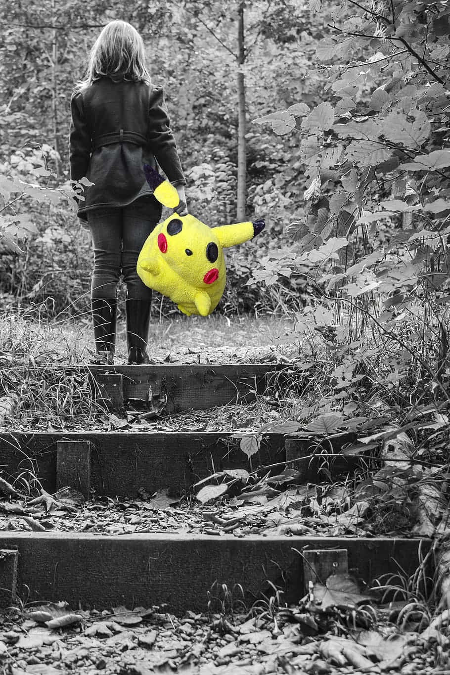 Pokemon Toys 桌布 壁紙 — 一個人在黑白森林背景下，拿著鮮黃色皮卡丘毛絨玩具走上森林階梯。