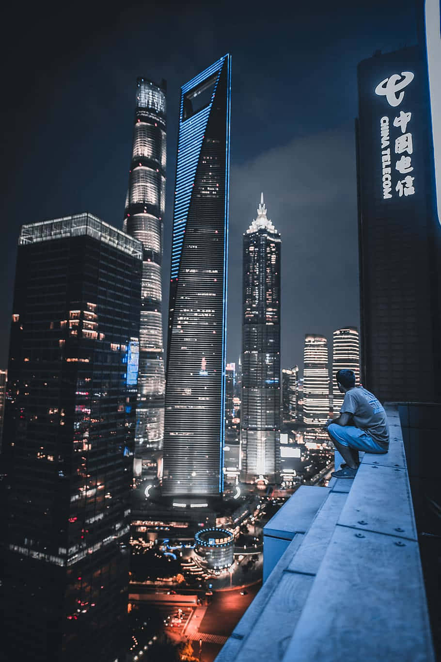 Rooftop 桌布 壁紙 — 一個人坐在屋頂邊緣，俯瞰著閃爍窗戶的摩天大樓所構成的迷人夜景。