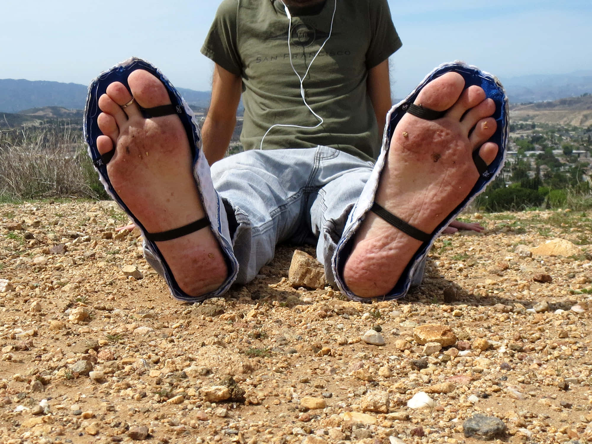 feet 桌布 壁紙 — 一個人坐在岩石地形上，雙腳穿著磨損的涼鞋朝向鏡頭，俯瞰著晴朗藍天下廣闊的山谷。