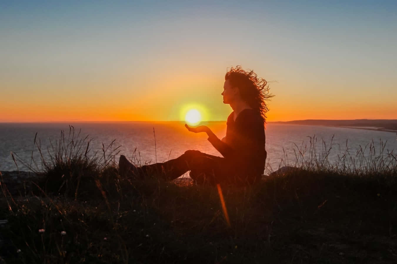 Alone 桌布 壁紙 — 一個人坐在日落時分的懸崖邊，雙手捧著，彷彿捧著發光的太陽在平靜的海洋上。