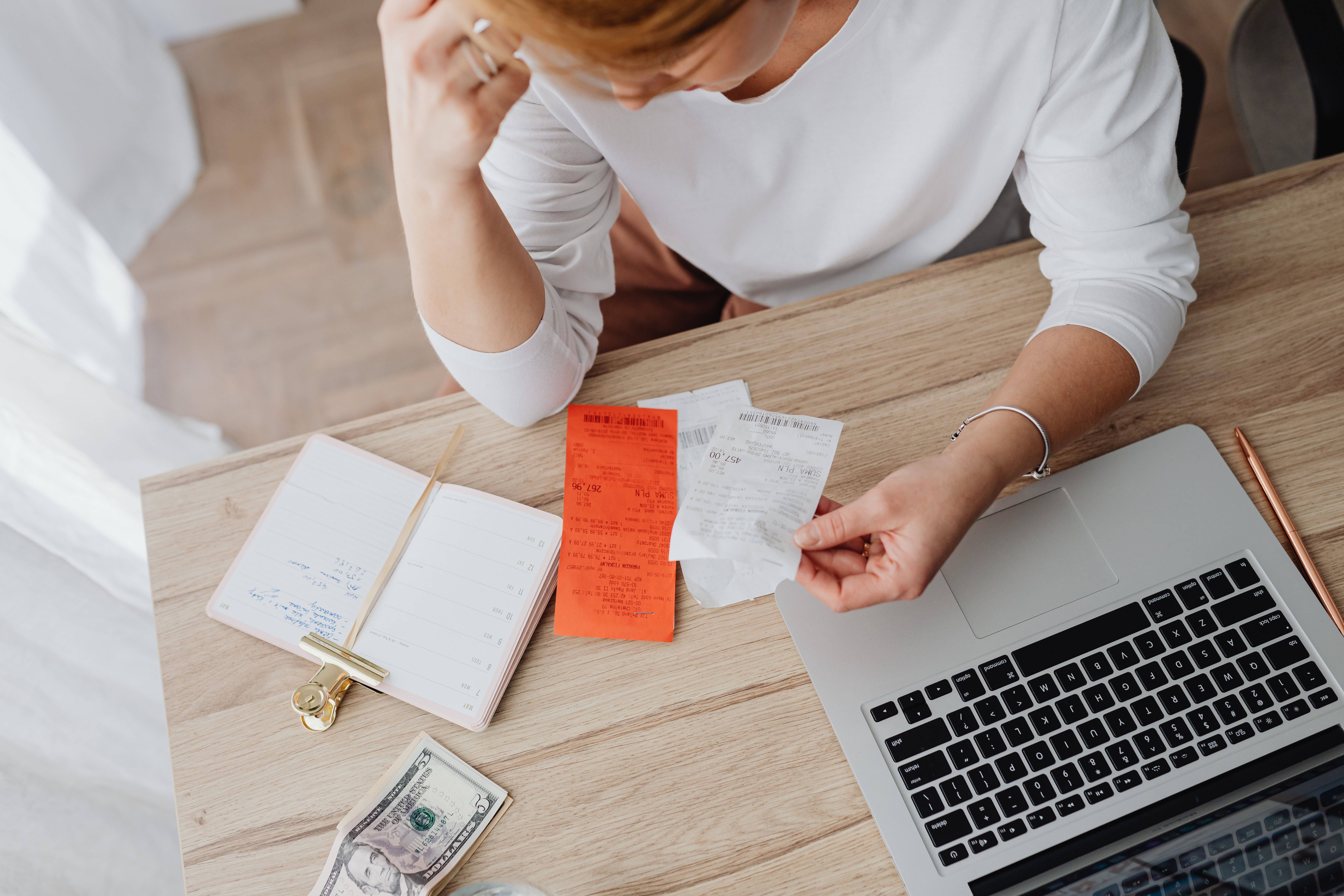 高清 桌布 壁紙 — 一個人坐在木桌前，一邊使用筆記型電腦進行預算或財務管理，一邊查看收據和現金。