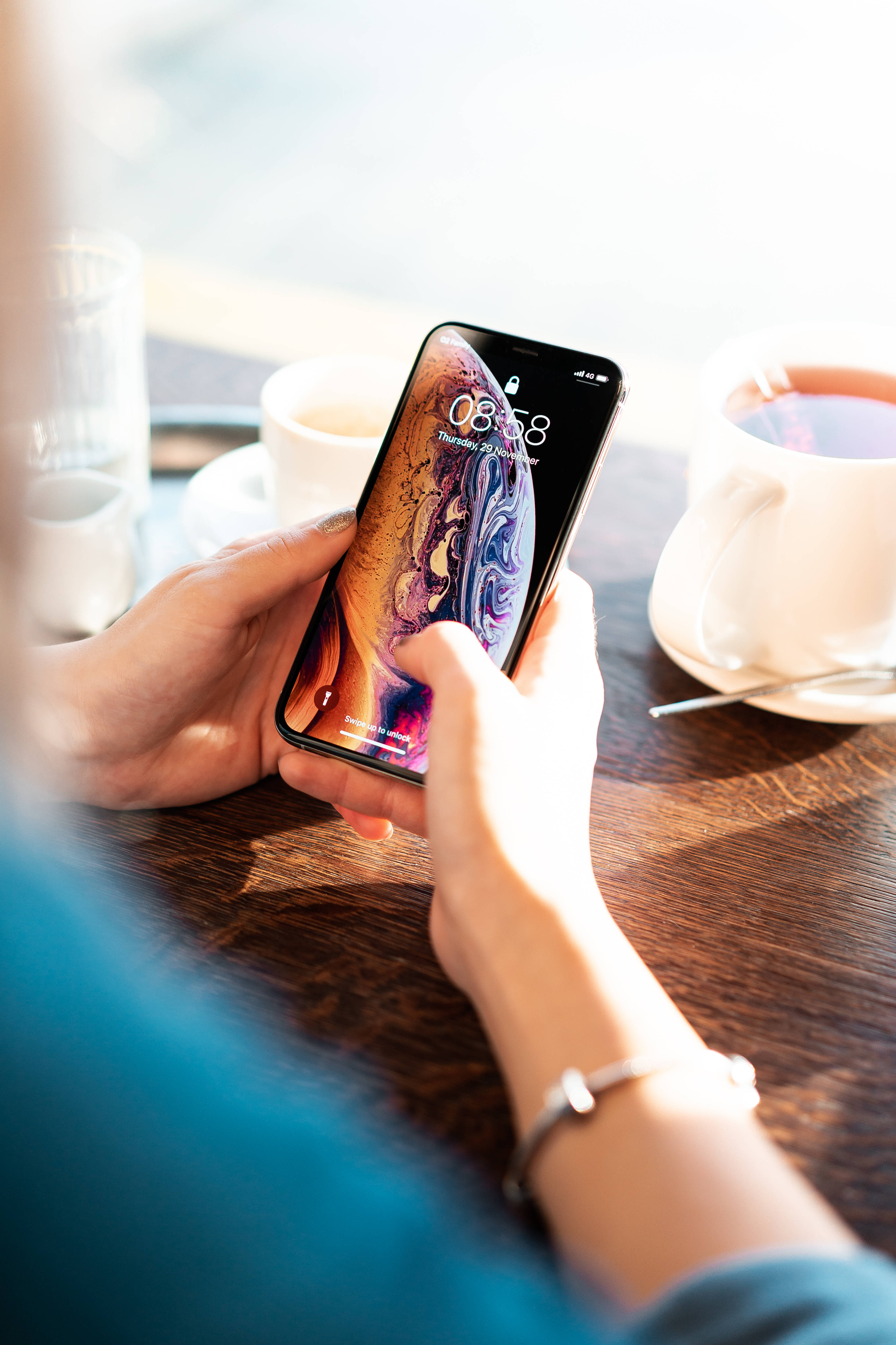 Apple iPhone 預設 桌布 壁紙 — 一個人坐在木桌旁，桌上放著咖啡杯，手持一部顯示色彩繽紛抽象桌布的智慧型手機。