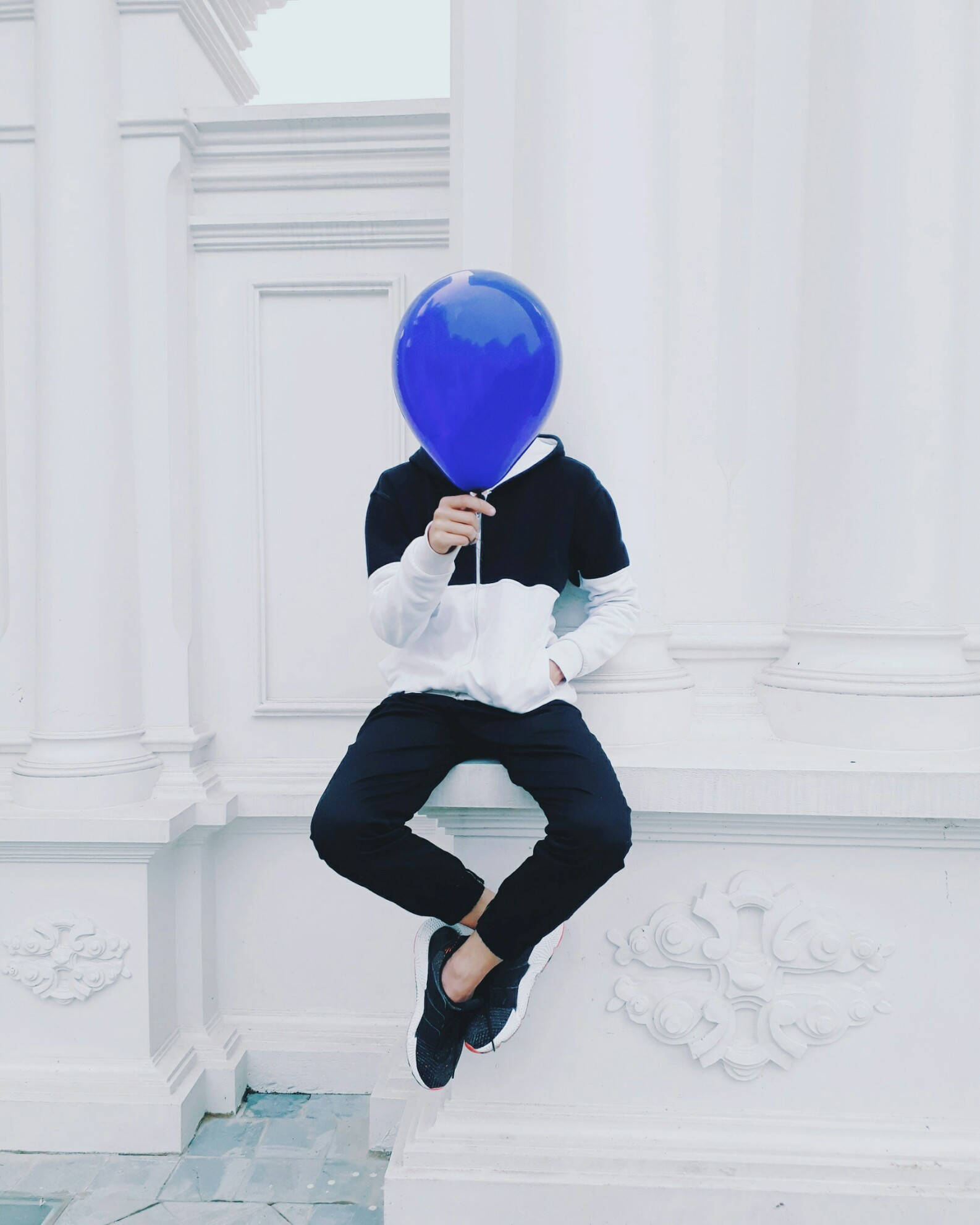 Balloon 桌布 壁紙 — 一個人坐在白色裝飾性窗台上，手持藍色氣球遮住臉部，背景是明亮的白色建築。