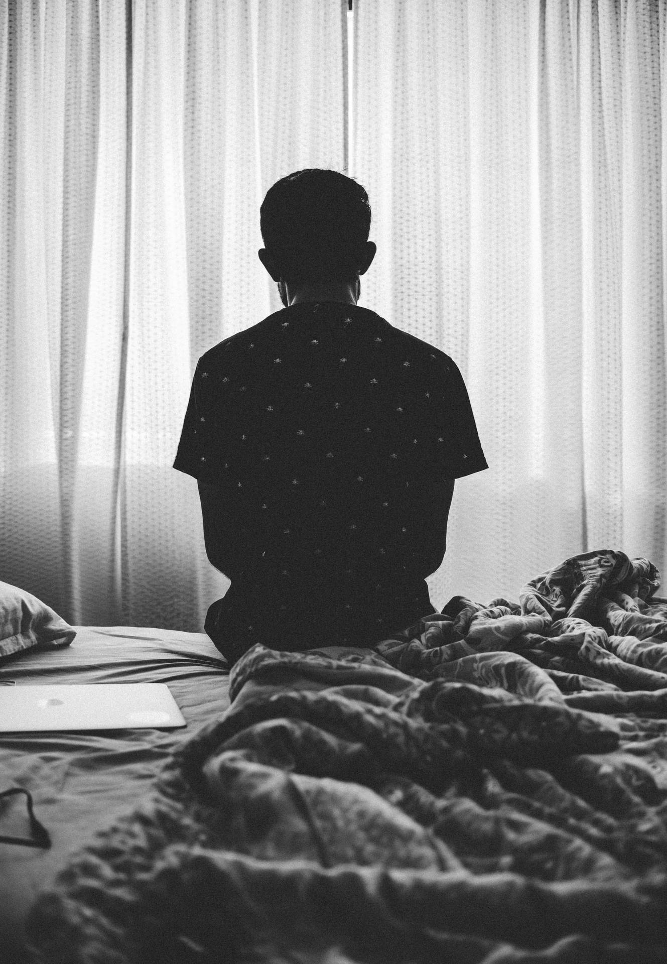一個人坐在床上面向窗簾的剪影，在寧靜的房間中。 — 單身男孩 壁紙