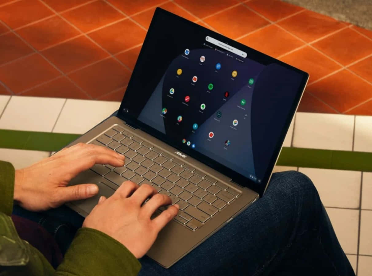 Chromebook 桌布 壁紙 — 一個人坐在磁磚地上，在銀色筆記型電腦上打字，螢幕上顯示色彩繽紛的應用程式圖示。
