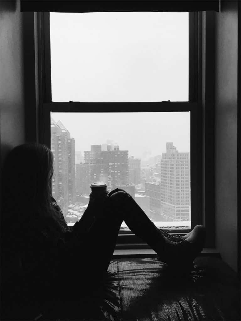 黑白美學動圖 桌布 壁紙 — 一個人坐在窗邊，手裡拿著杯子，凝視著單色朦朧的城市景觀的剪影。
