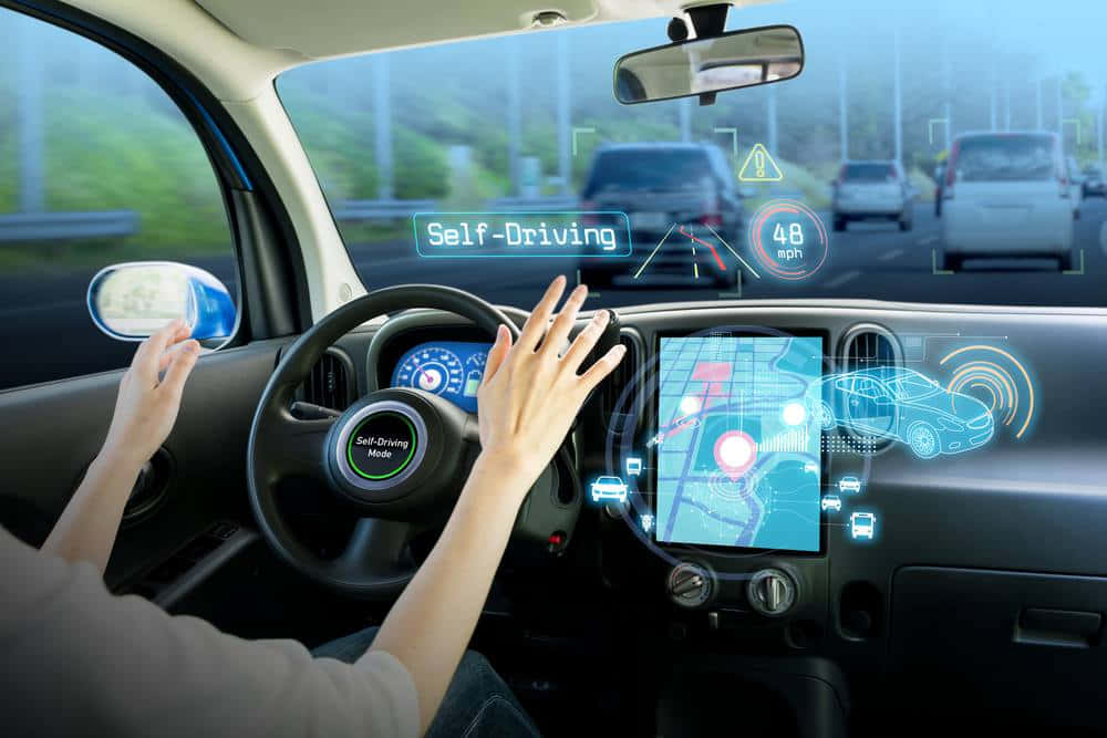 Car Technology 桌布 壁紙 — 一個人坐在自動駕駛汽車中，雙手離開方向盤，儀表板上的全息顯示屏顯示導航和車輛狀態。