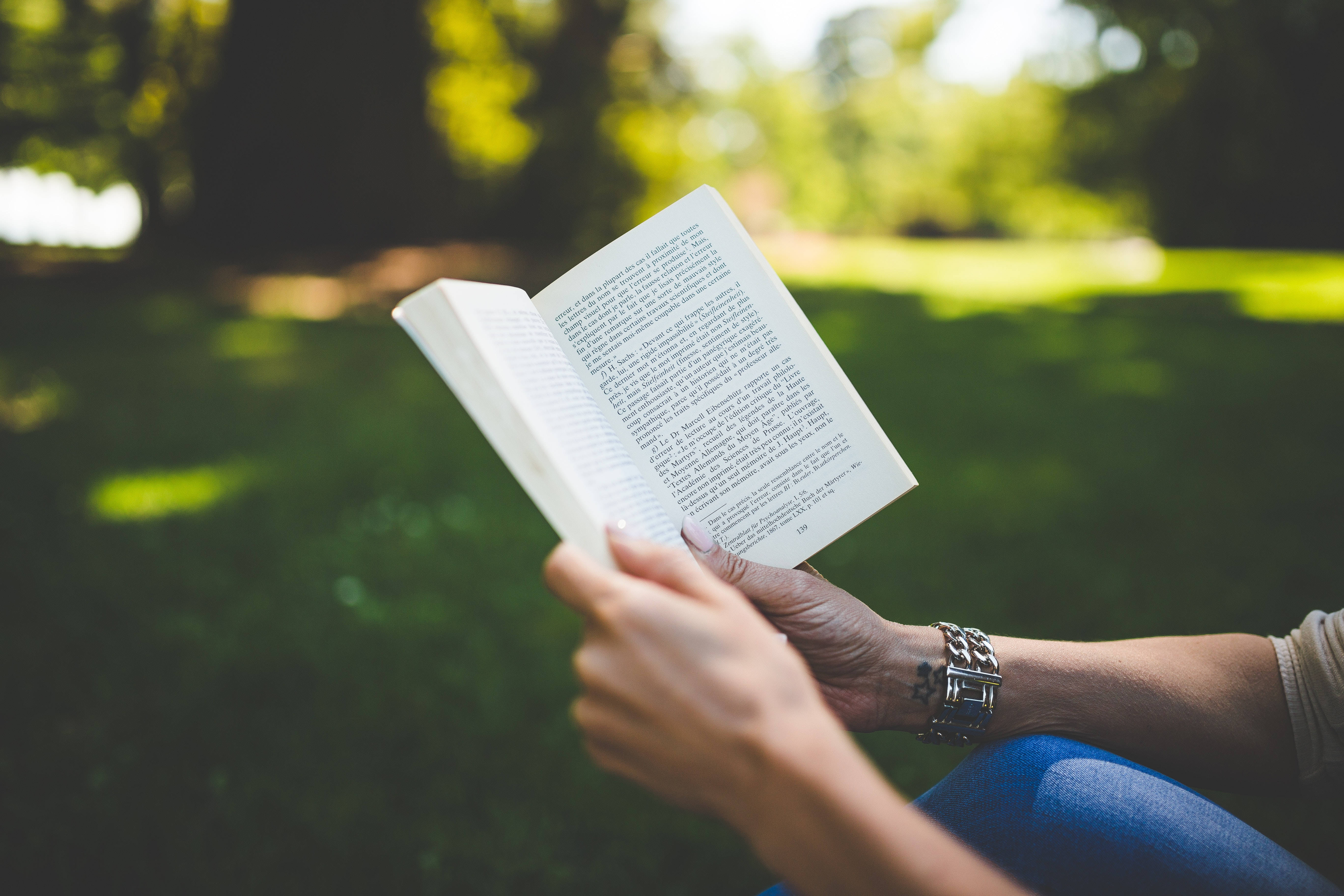 Reading 桌布 壁紙 — 一個人坐在草地上，在斑駁的陽光下看書，背景有柔焦的樹木。