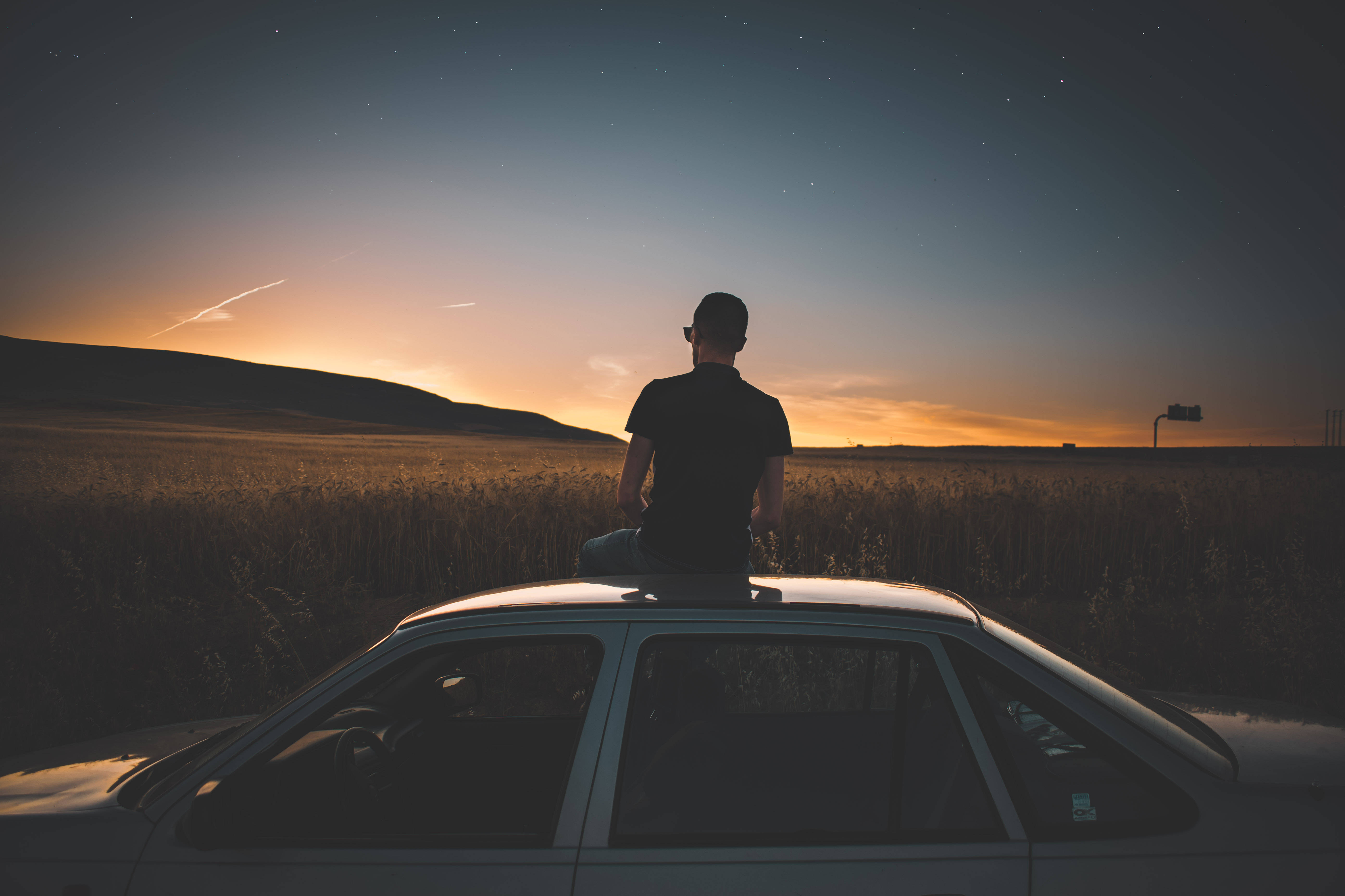 Chill 桌布 壁紙 — 一個人坐在金色田野中的車頂上，凝視著星光燦爛的黃昏天空和遠山。