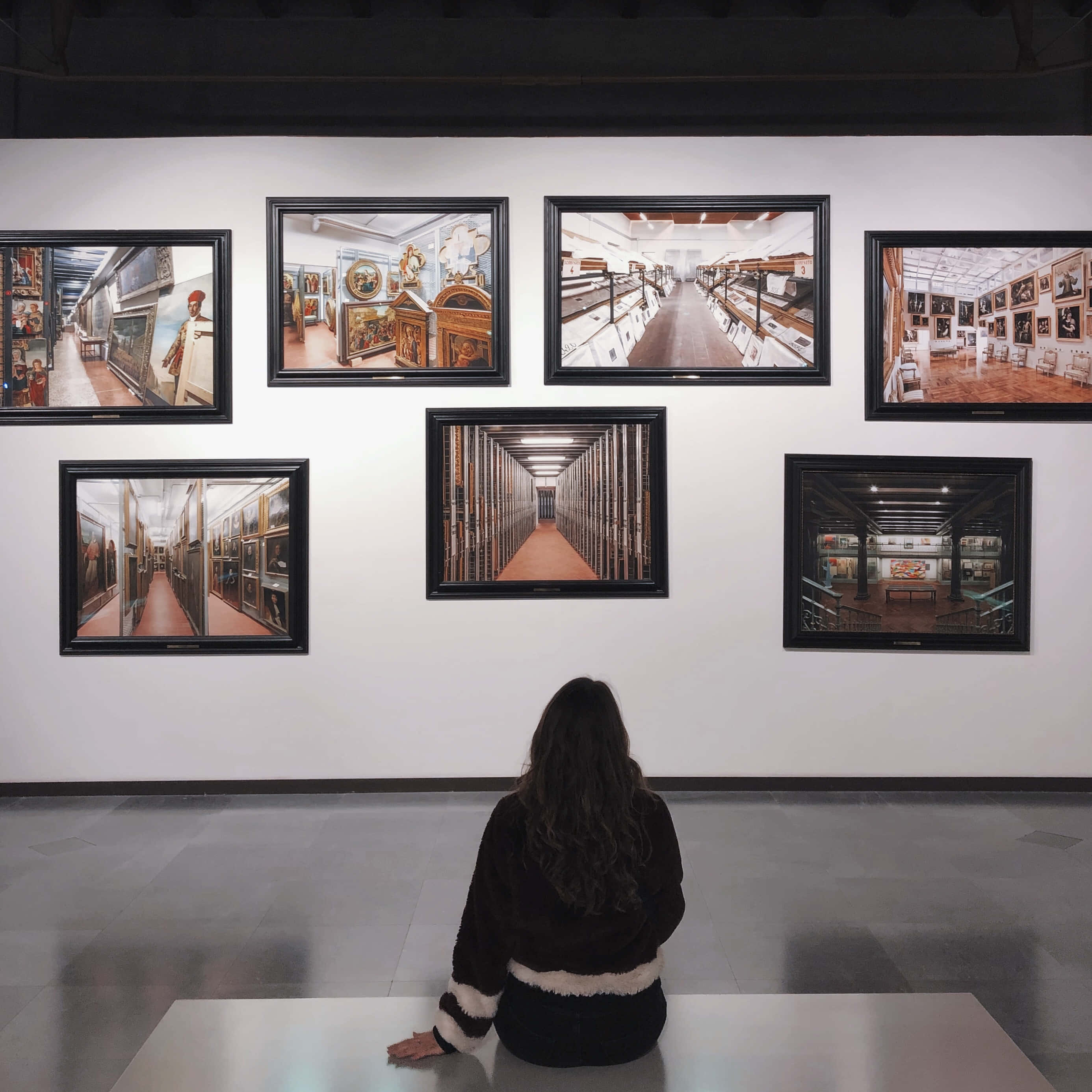 Museum 桌布 壁紙 — 一個人坐在長椅上，面向一幅掛滿裱框照片的牆壁，照片展示博物館內部及文物。