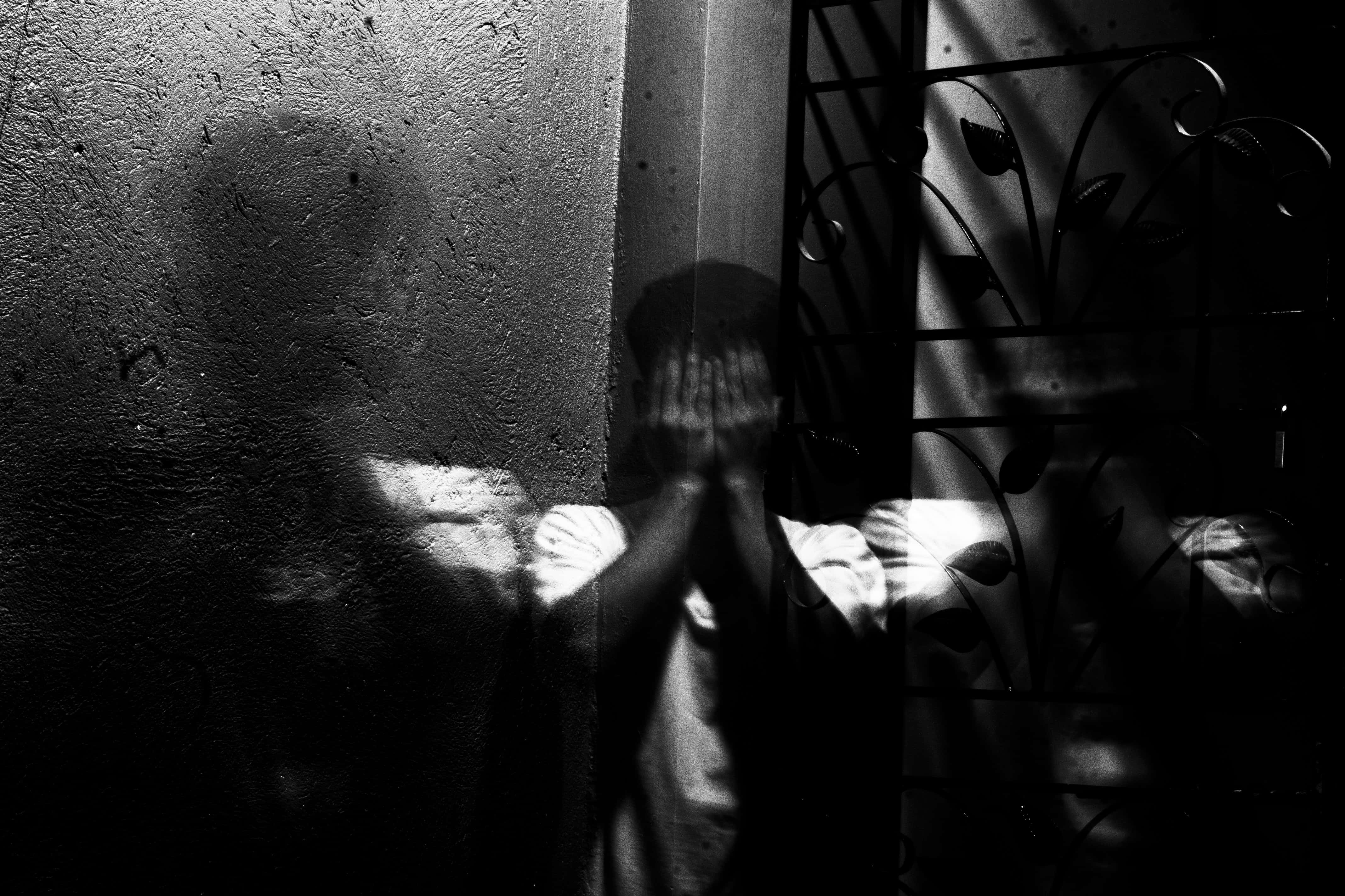 Dark Fear 桌布 壁紙 — 一個人將手按在玻璃門上，在紋理牆壁上投射出扭曲的影子，高對比度黑白。