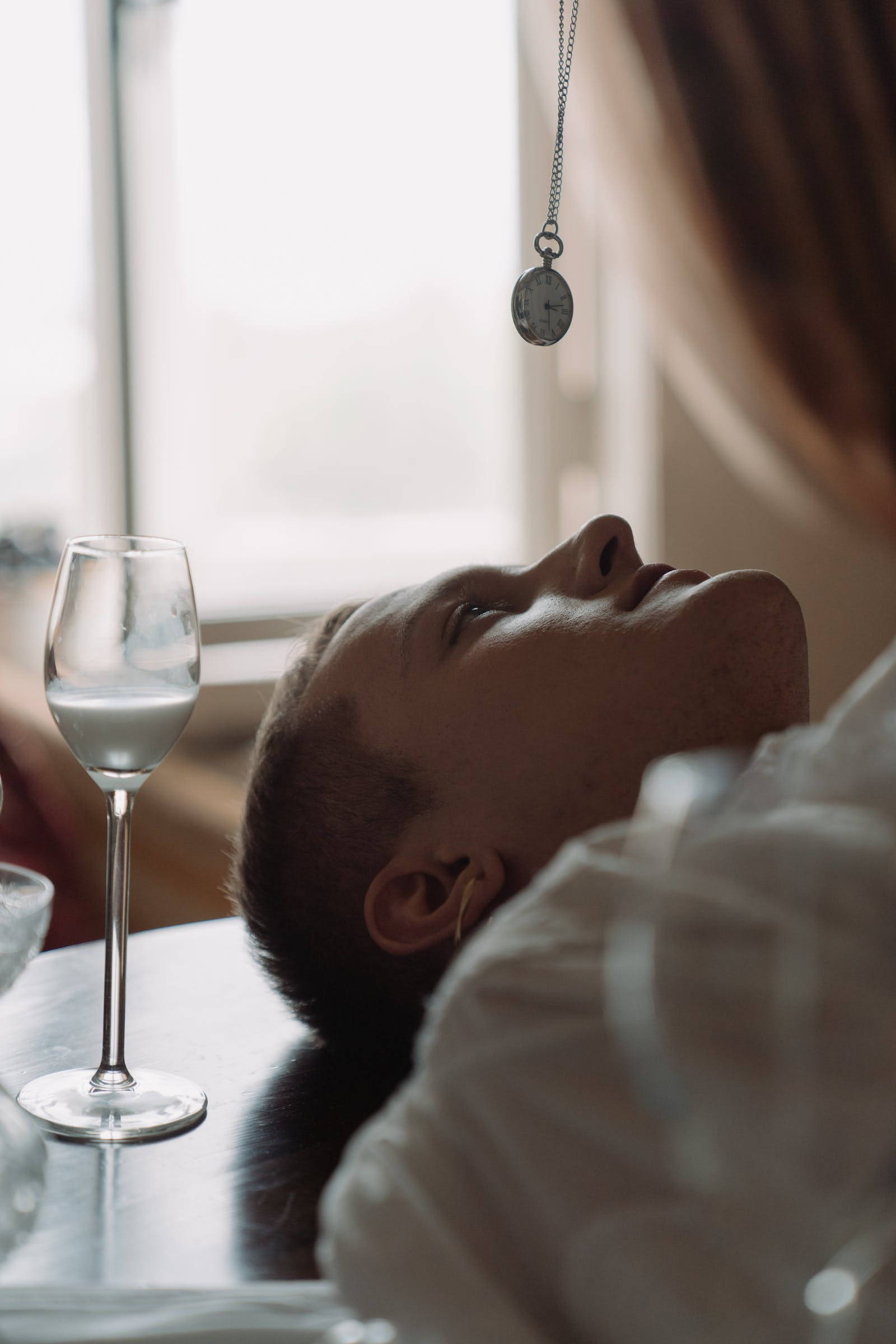 Hypnosis 桌布 壁紙 — 一個人將頭靠在桌子上，抬頭看著掛在酒杯旁邊的懷錶。