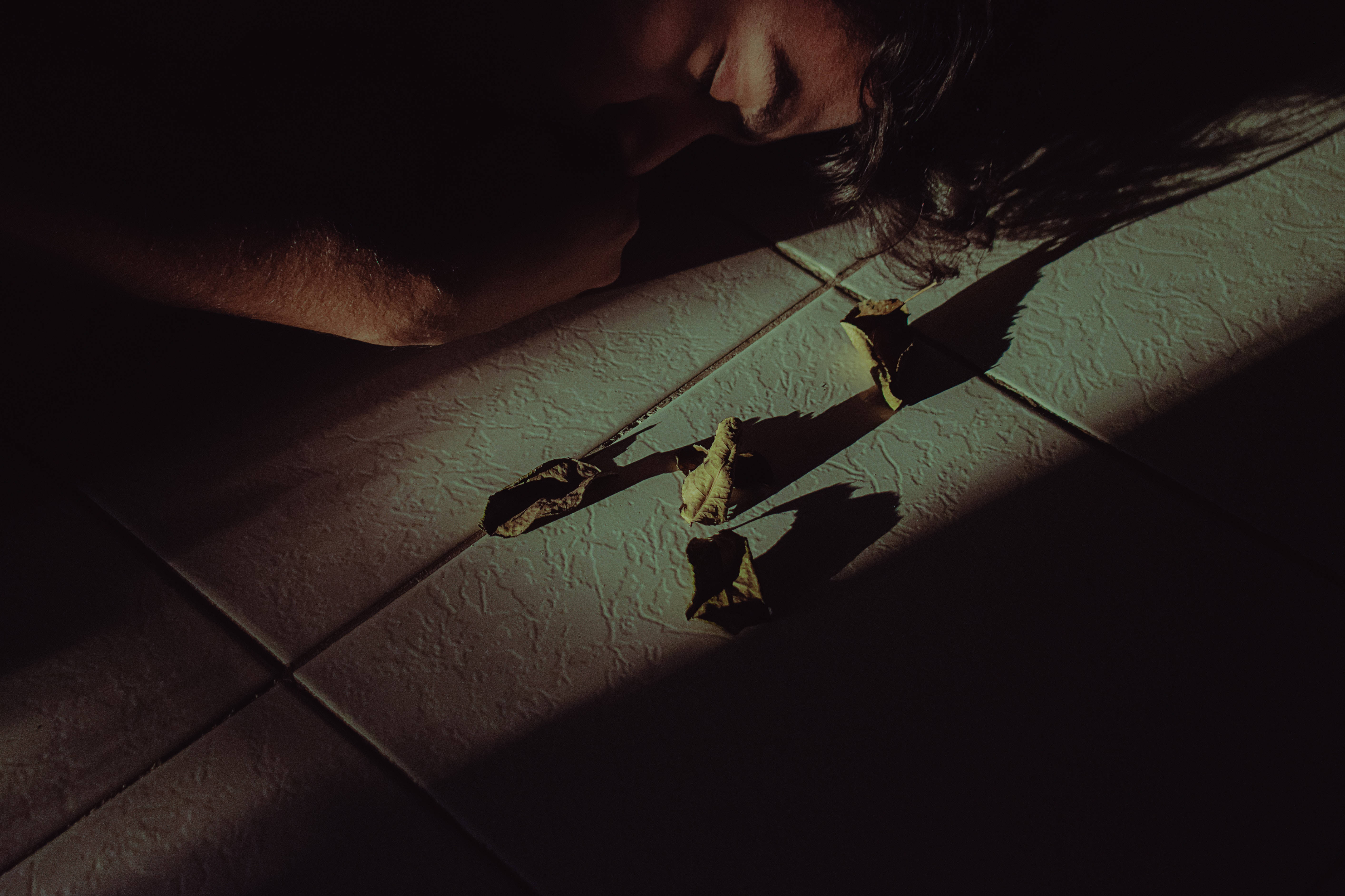Depression Aesthetic 桌布 壁紙 — 一個人將頭靠在磁磚地板上，一道光束照亮了附近的乾樹葉。