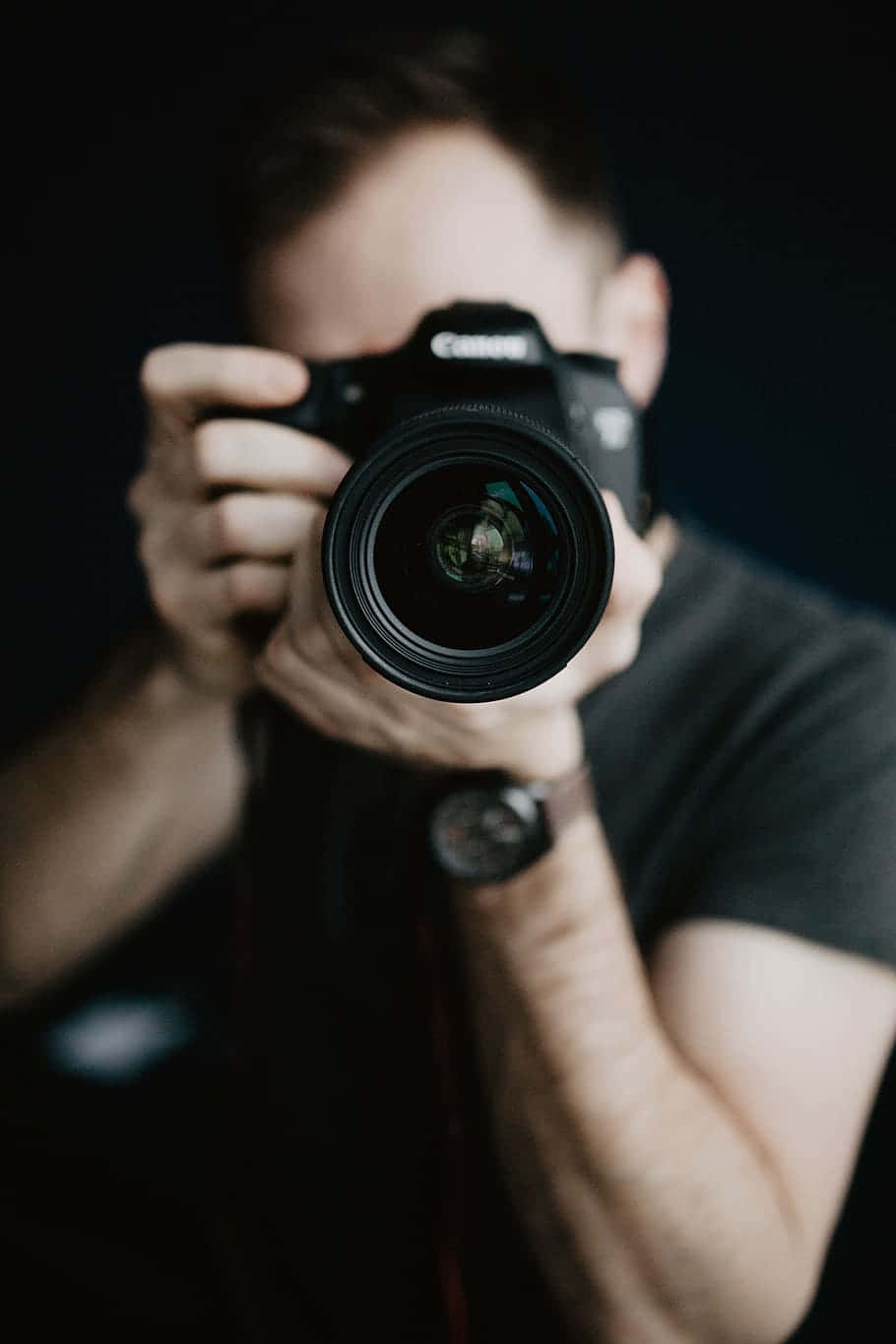 Dslr 桌布 壁紙 — 一個人將黑色單眼相機舉到臉前，背景昏暗且景深較淺。