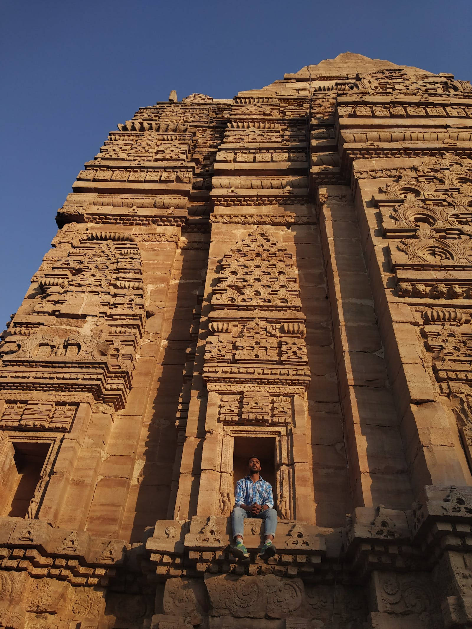 Hindu Temple 桌布 壁紙 — 一個人平靜地坐在一座雕刻精細的古老寺廟的石台上，背景是清澈的藍天。