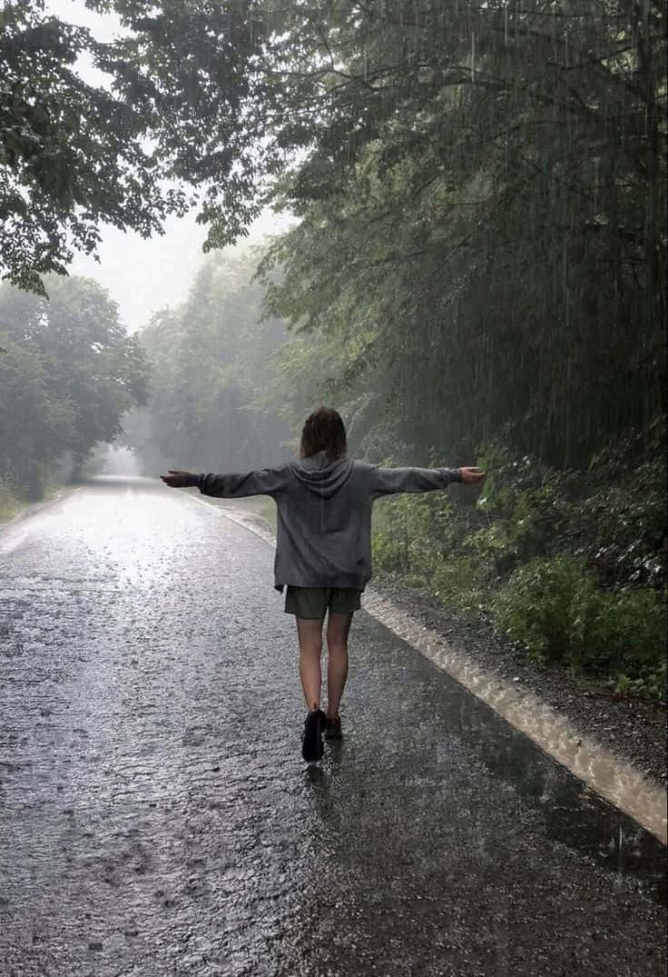 Rainy Day 桌布 壁紙 — 一個人張開雙臂，走在被雨水浸濕的森林小路上，周圍是茂密的綠樹。