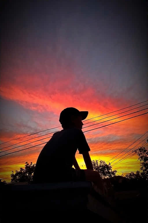 Rooftop Reverie Sunset Colors 4K 壁紙 — 一個人影坐在建築物頂部，觀看帶有電線橫跨天空的火橙色和紫色日落。