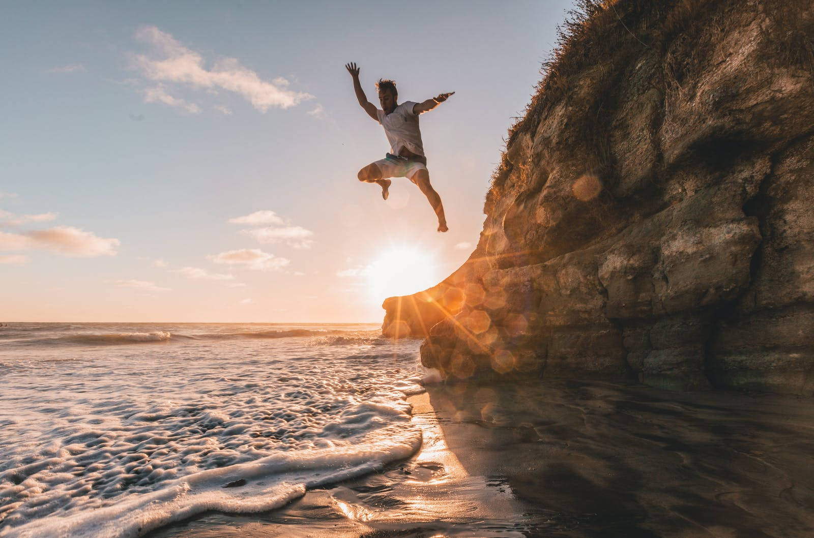 Jumping 桌布 壁紙 — 一個人從懸崖上歡快地跳入海洋，金色夕陽的光芒在他們身後閃耀。