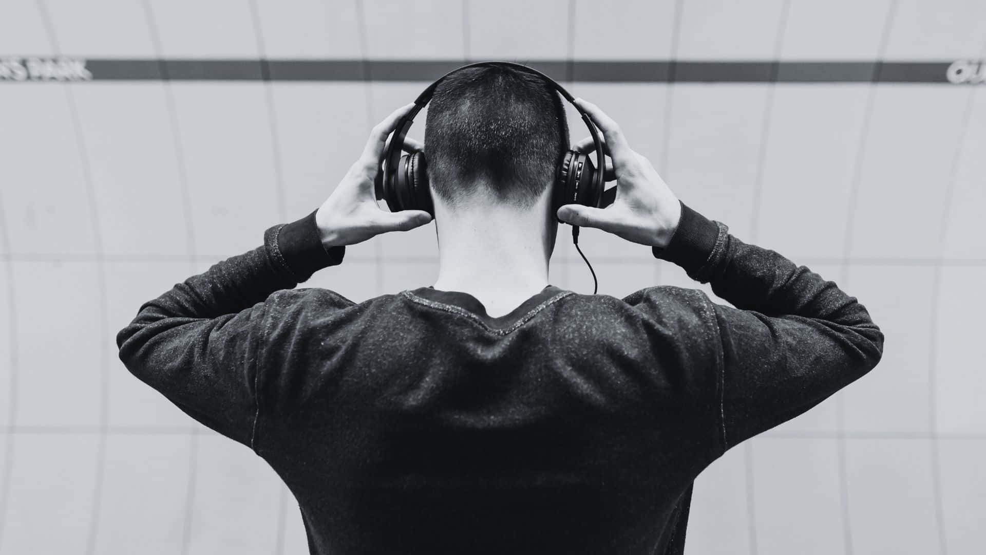 Black And White Music 桌布 壁紙 — 一個人從背後調整頭戴式耳機，背景是磁磚牆，黑白風格。